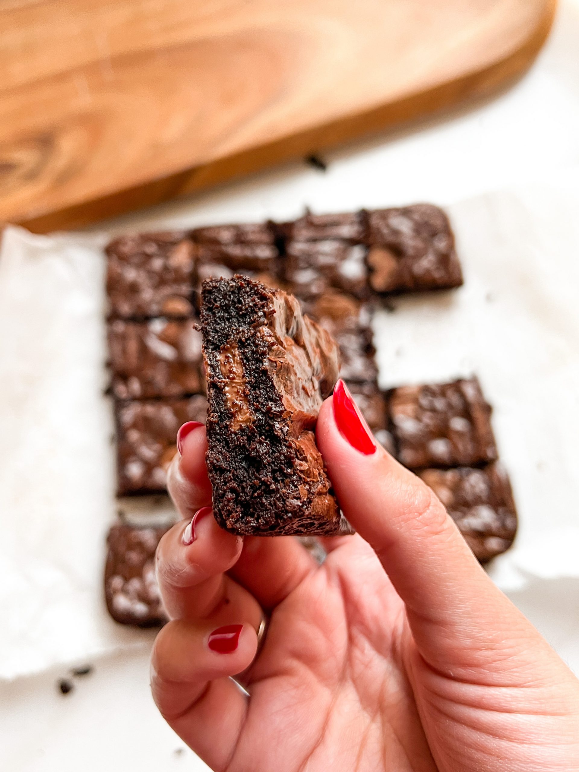 Hand holding a brownie sideways to show dark, fudgy interior with melting chocolate, with remaining brownies in the background