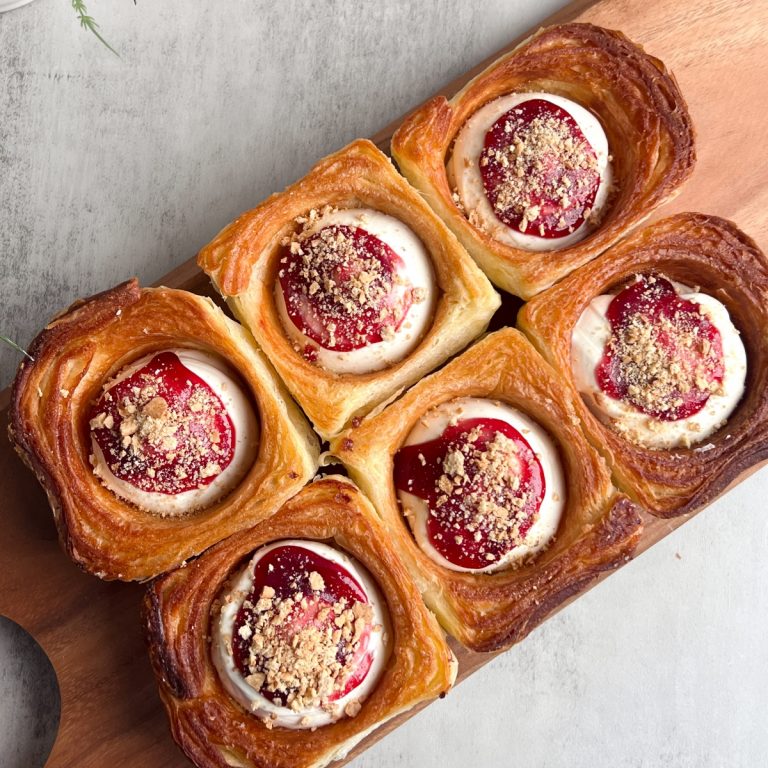 Overhead shot of 6 croissant cups filled with cheesecake filling, topped with red raspberry glaze and crushed graham crackers