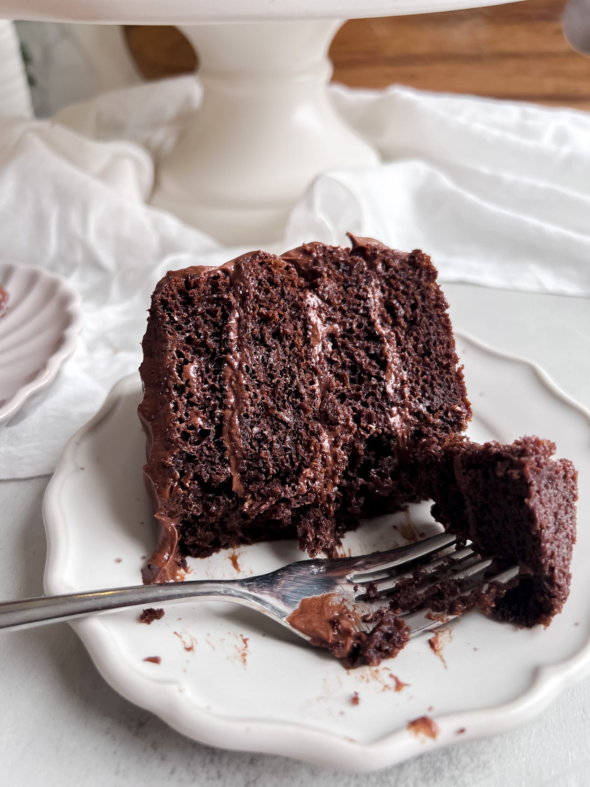 Close up shot of a slice of chocolate cake on a small plate with a fork taking out a bite