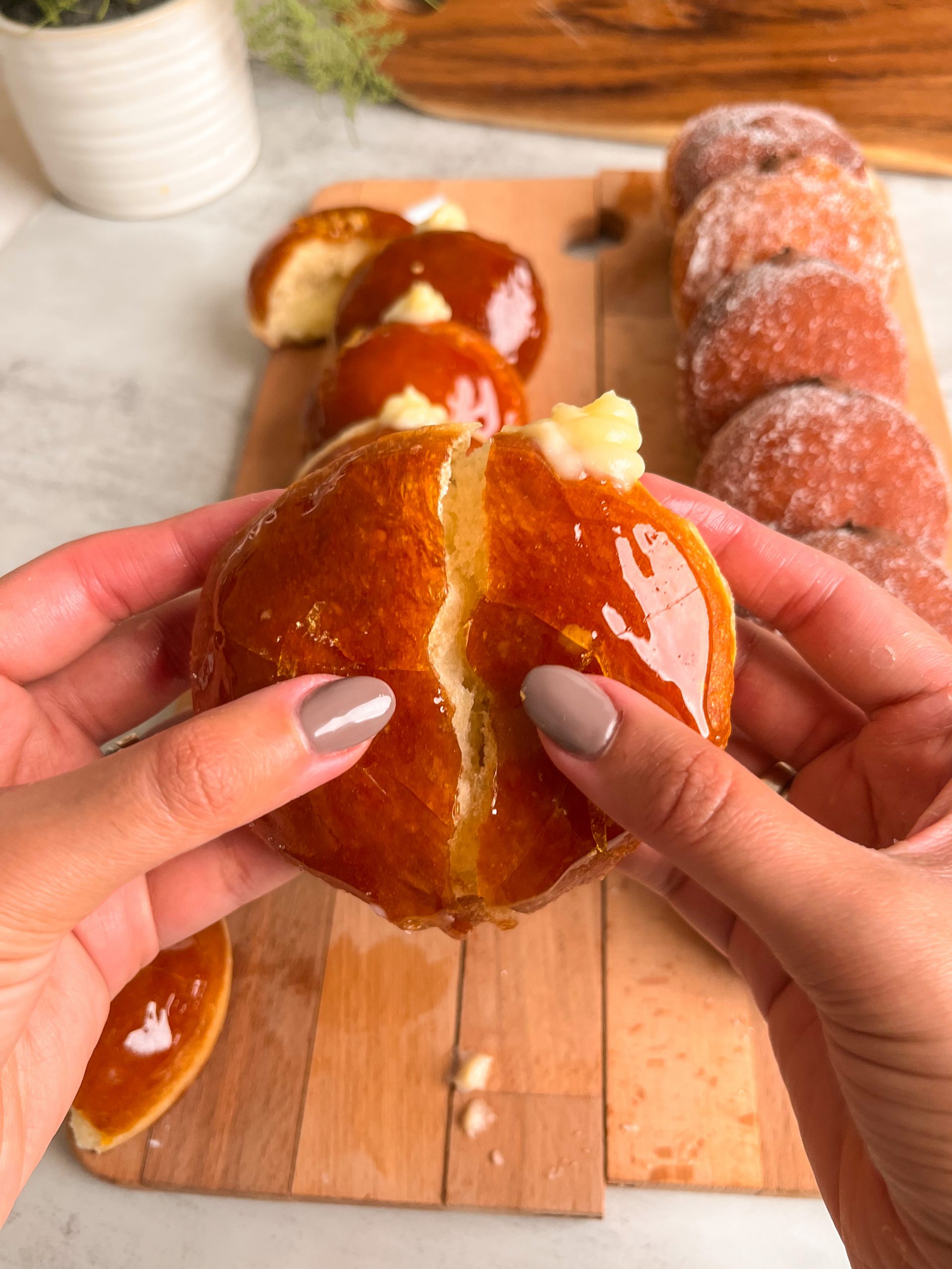 Two hands pulling apart a creme brulee donut, with the caramel coating cracked where the donut is being halved