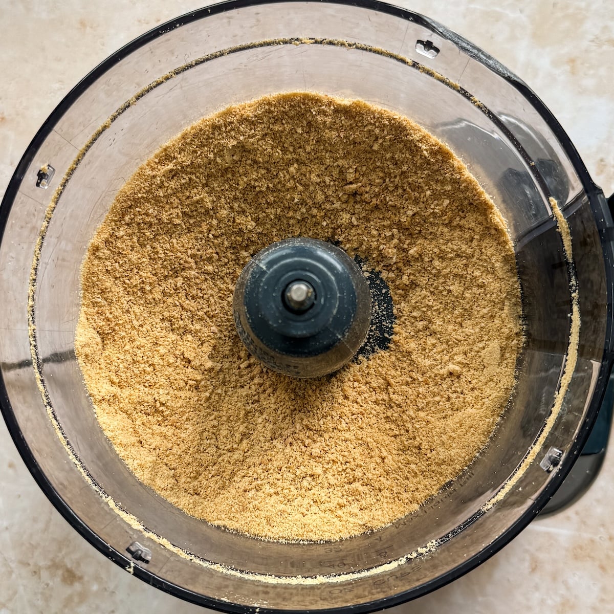 A food processor bowl filled with finely ground graham crackers viewed from above.