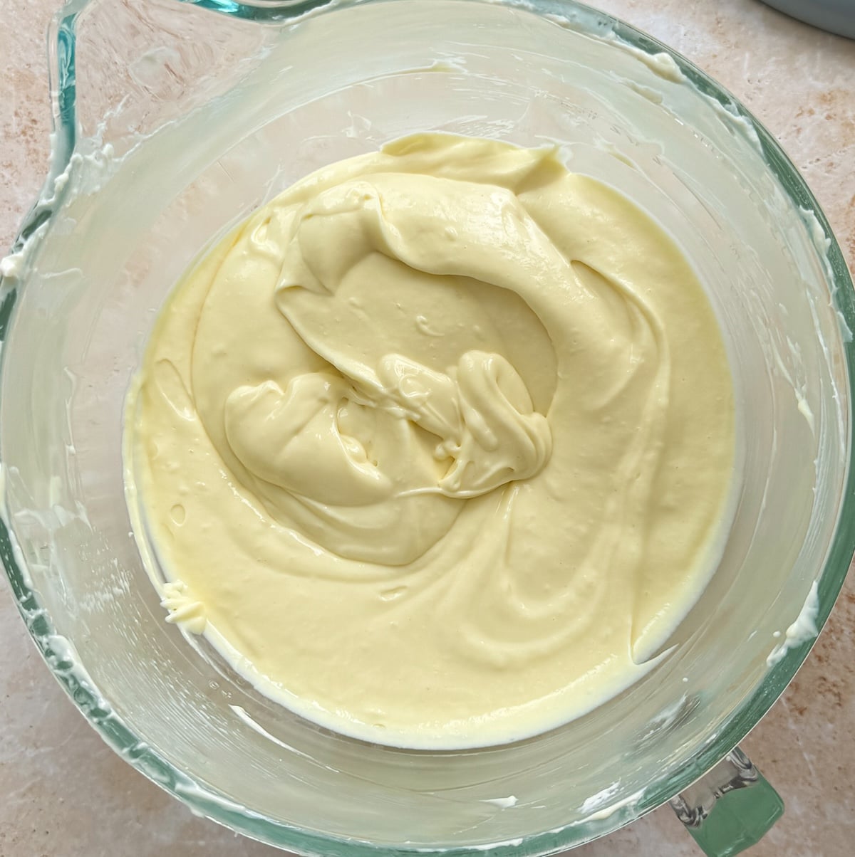 Thick, creamy yellow cheesecake batter with eggs mixed in, in a glass mixing bowl on a light countertop