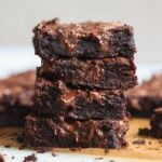 A stack of four gooey chocolate brownies with melted chocolate oozing out, placed on a parchment-lined wooden board