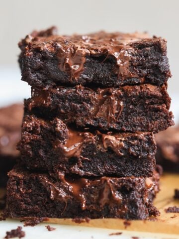 A stack of four gooey chocolate brownies with melted chocolate oozing out, placed on a parchment-lined wooden board