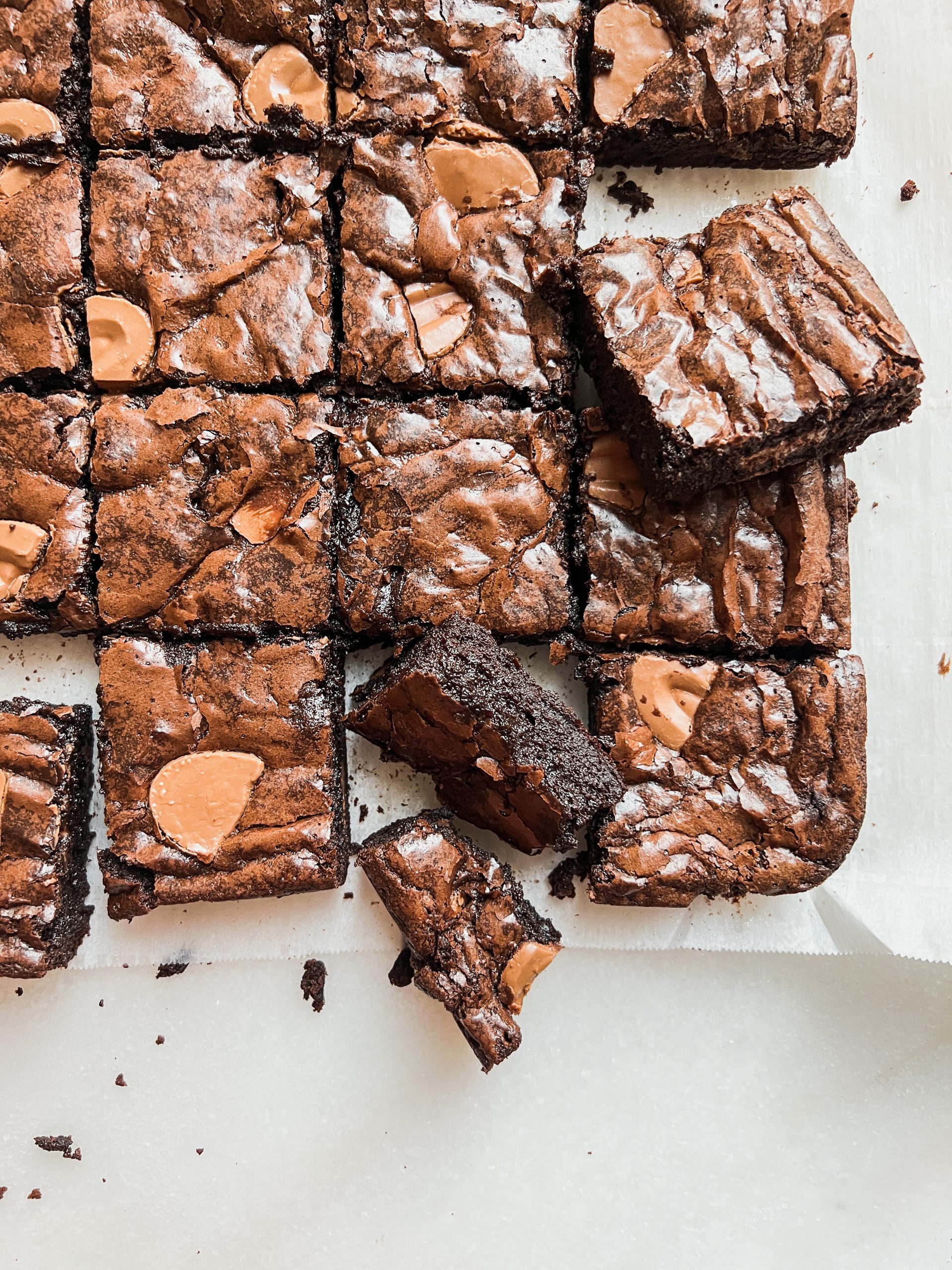 Zoomed picture of a tray of brownies, with some brownies placed sideways and some showing partially. Brownies have shiny crinkly top and dark chocolatey fudgy interior