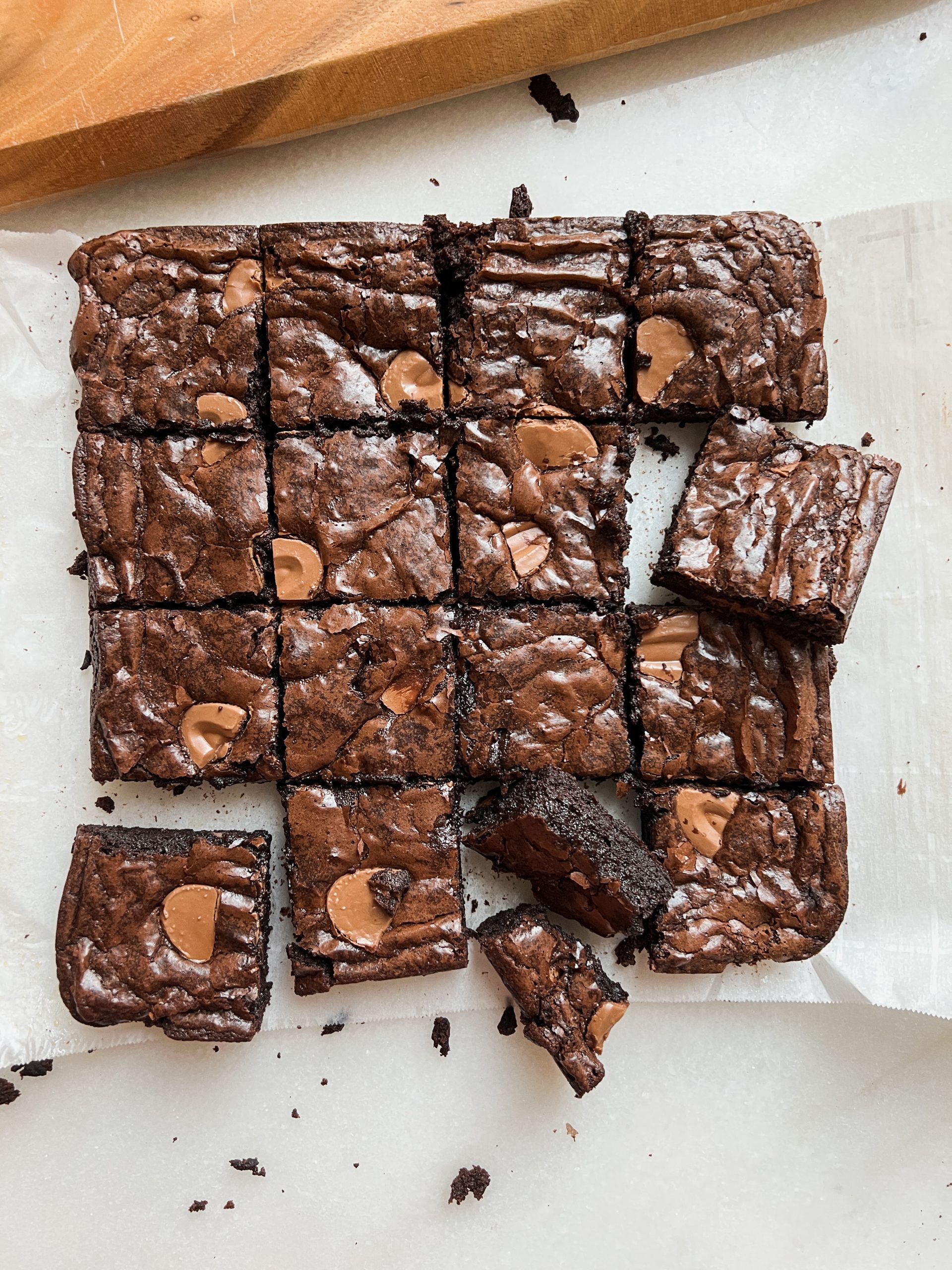 Overhead picture of sliced brownies on parchment paper. Brownies have shiny crinkly top and fudgy interior with chopped chocolate throughout. Three brownies are placed haphazarly