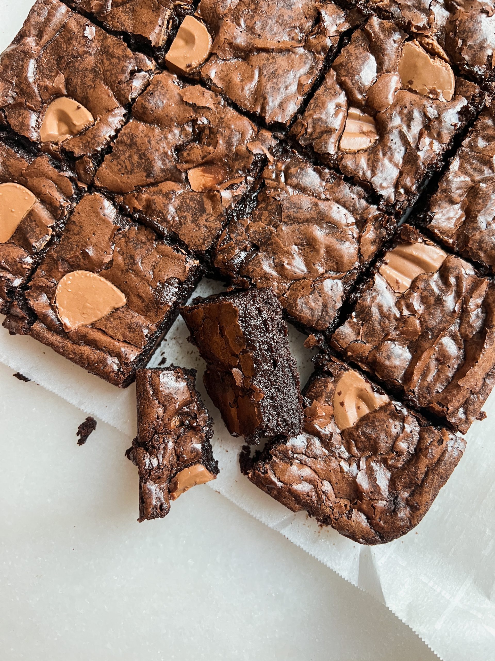 Overhead shot of brownies with shiny crinkly top, one brownie angled to show dark fudgy interior