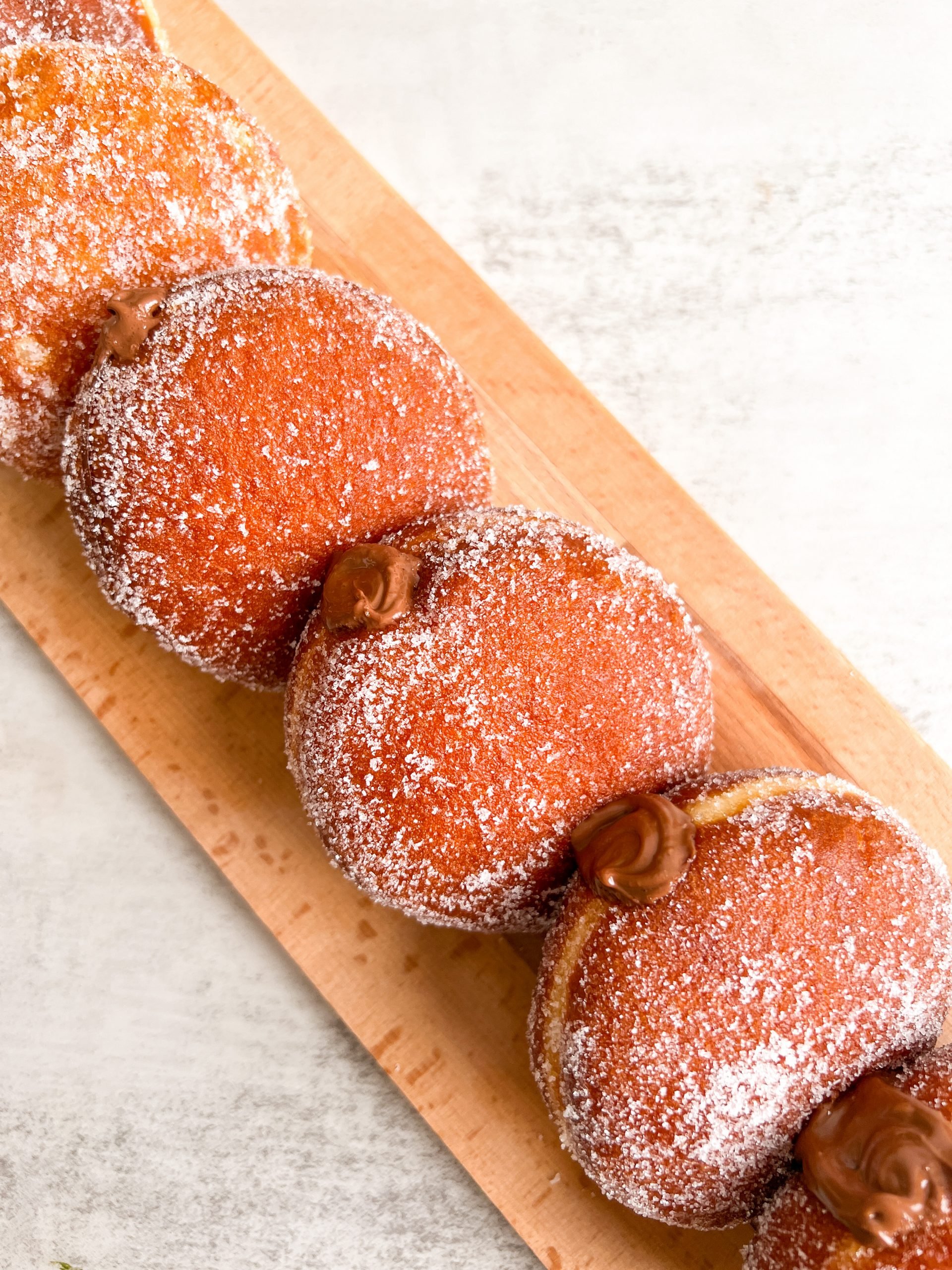 Overhead shot of 3 nutella donuts stacked in a line. Donuts are coated in sugar and nutella can be seen ozzing out of them from the top