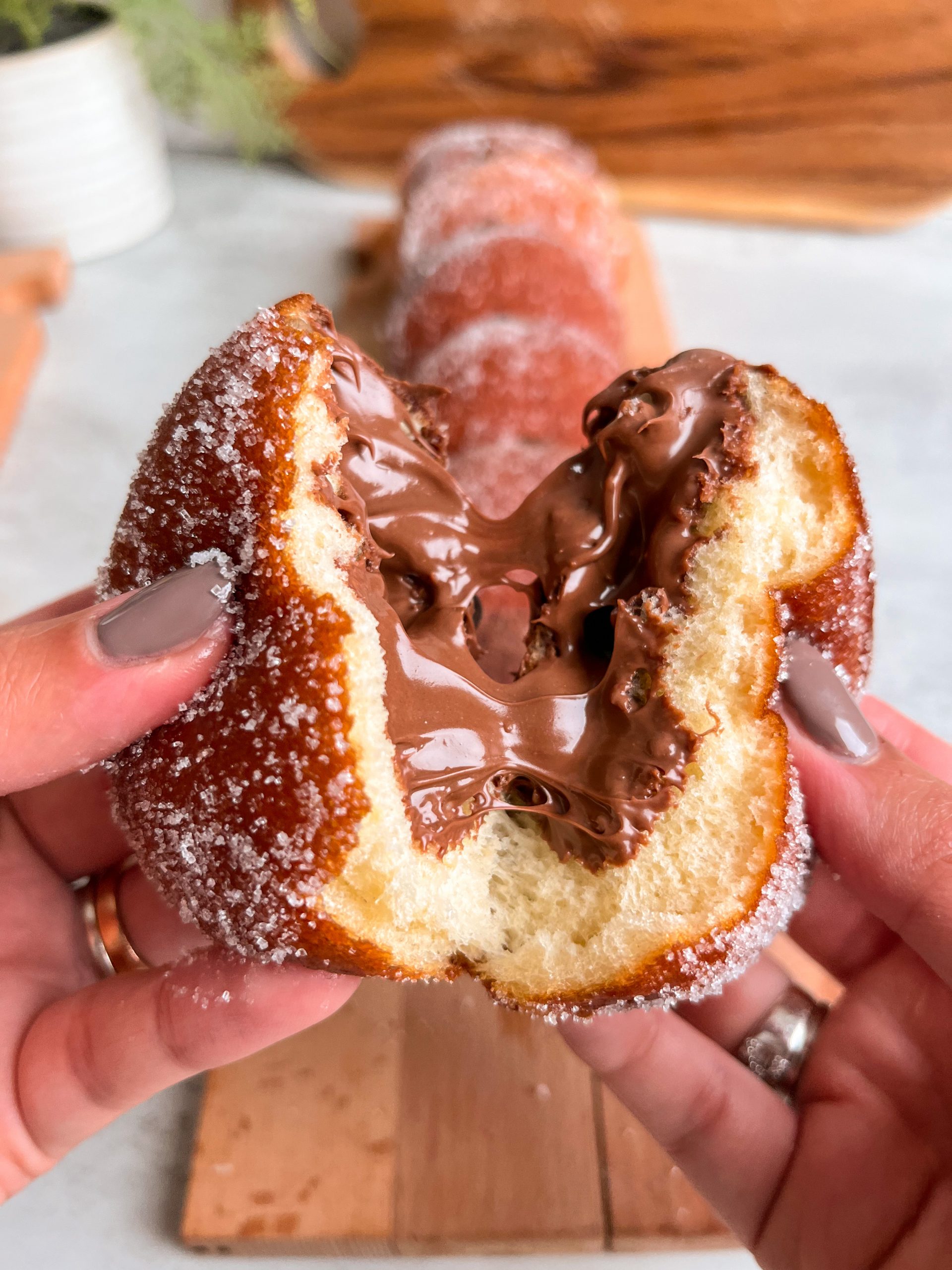 Two hands pulling a donut into two halves with nutella oozing out of it