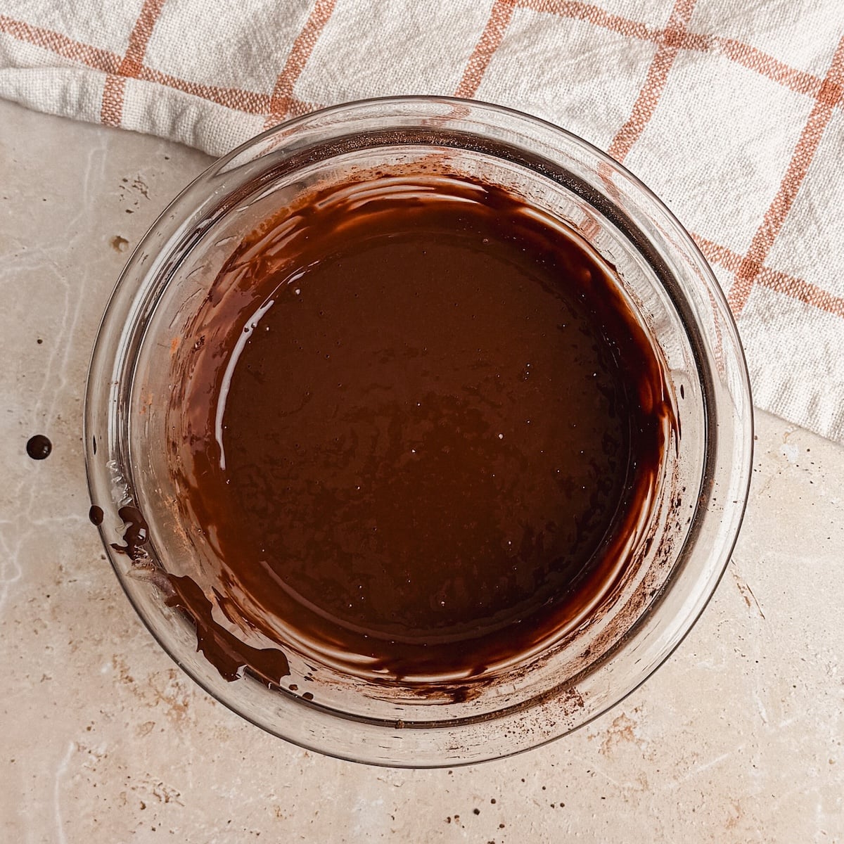 A glass bowl filled with smooth, cocoa powder mixture sits on a light countertop next to a white and orange checkered cloth