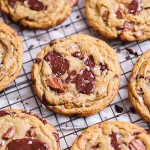 brown butter chocolate chip cookies on a wire rack. they are thick and golden, crispy on the outside with lots of melted chocolate puddles and sprinkled with sea salt. focus on one cookie