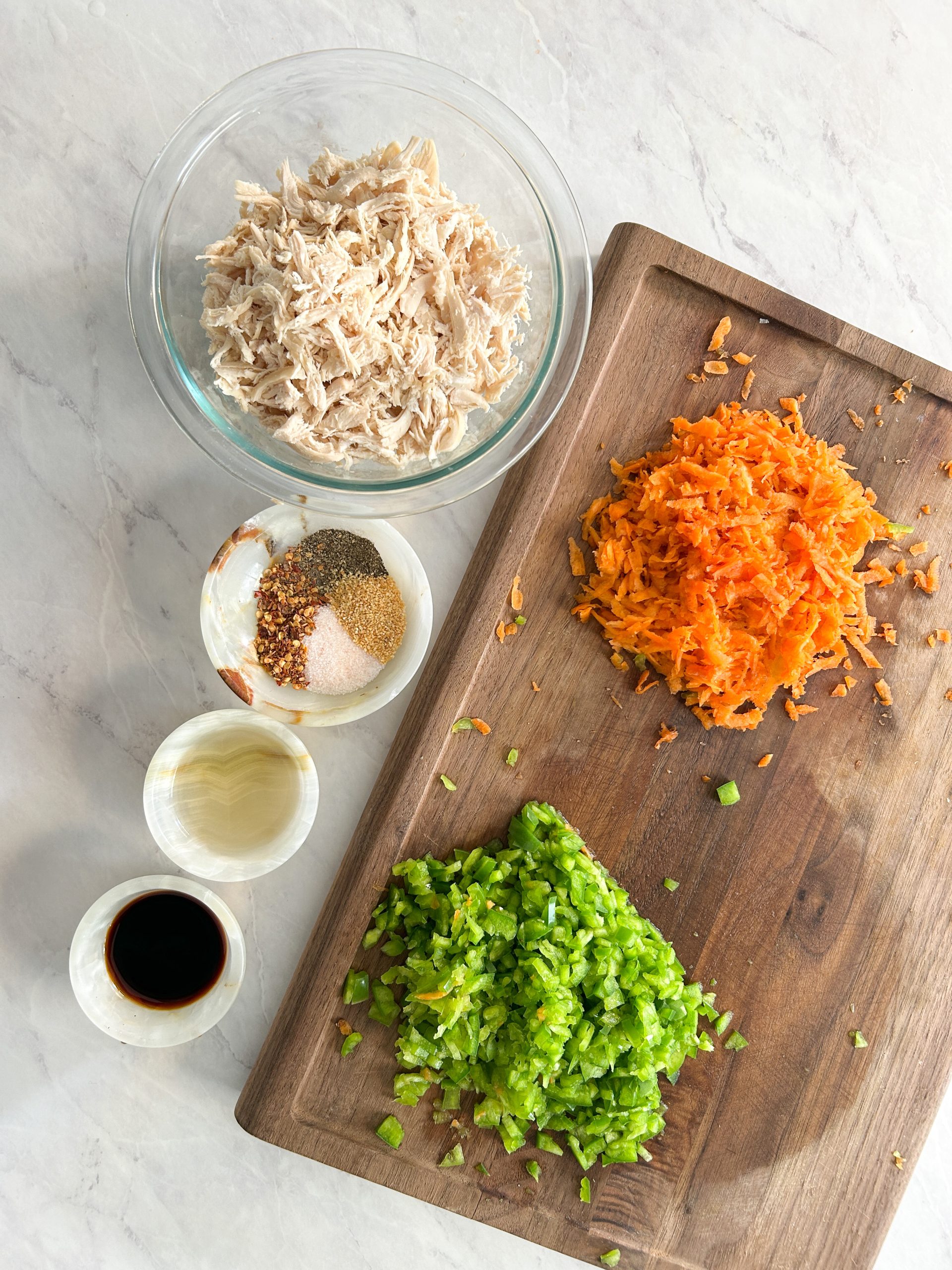 array of ingredients: shredded chicken, carrots, bell peppers, spices and condiments