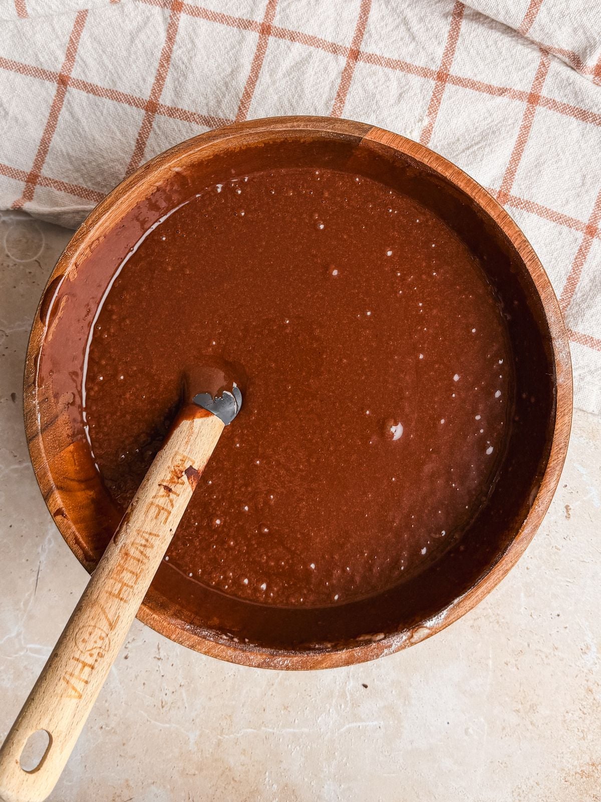 chocolate cake batter in a wooden bowl with a rubber spatula resting in it