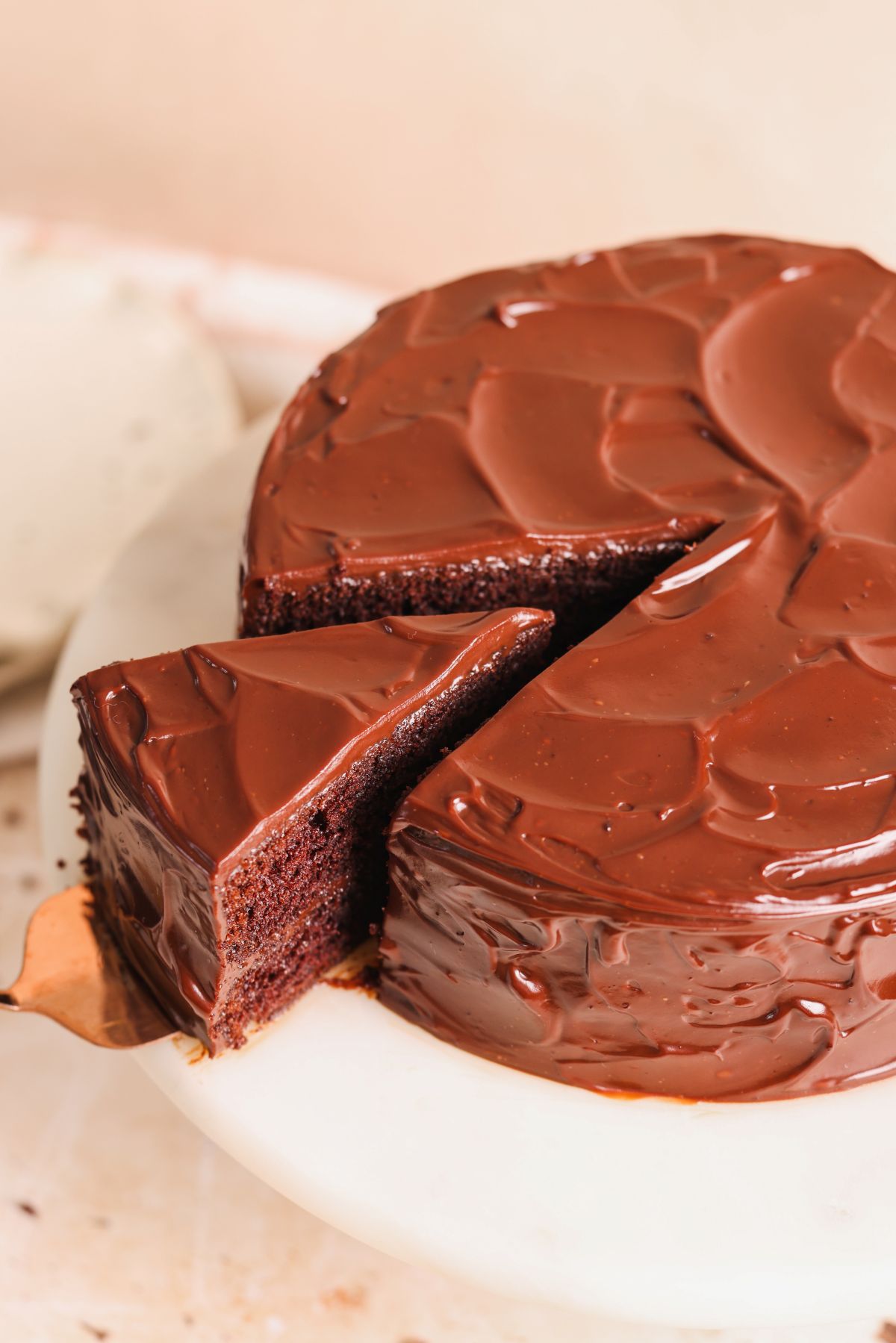 a spatula pulling out a slice of chocolate cake from it on a marble cake stand, pictured from the top