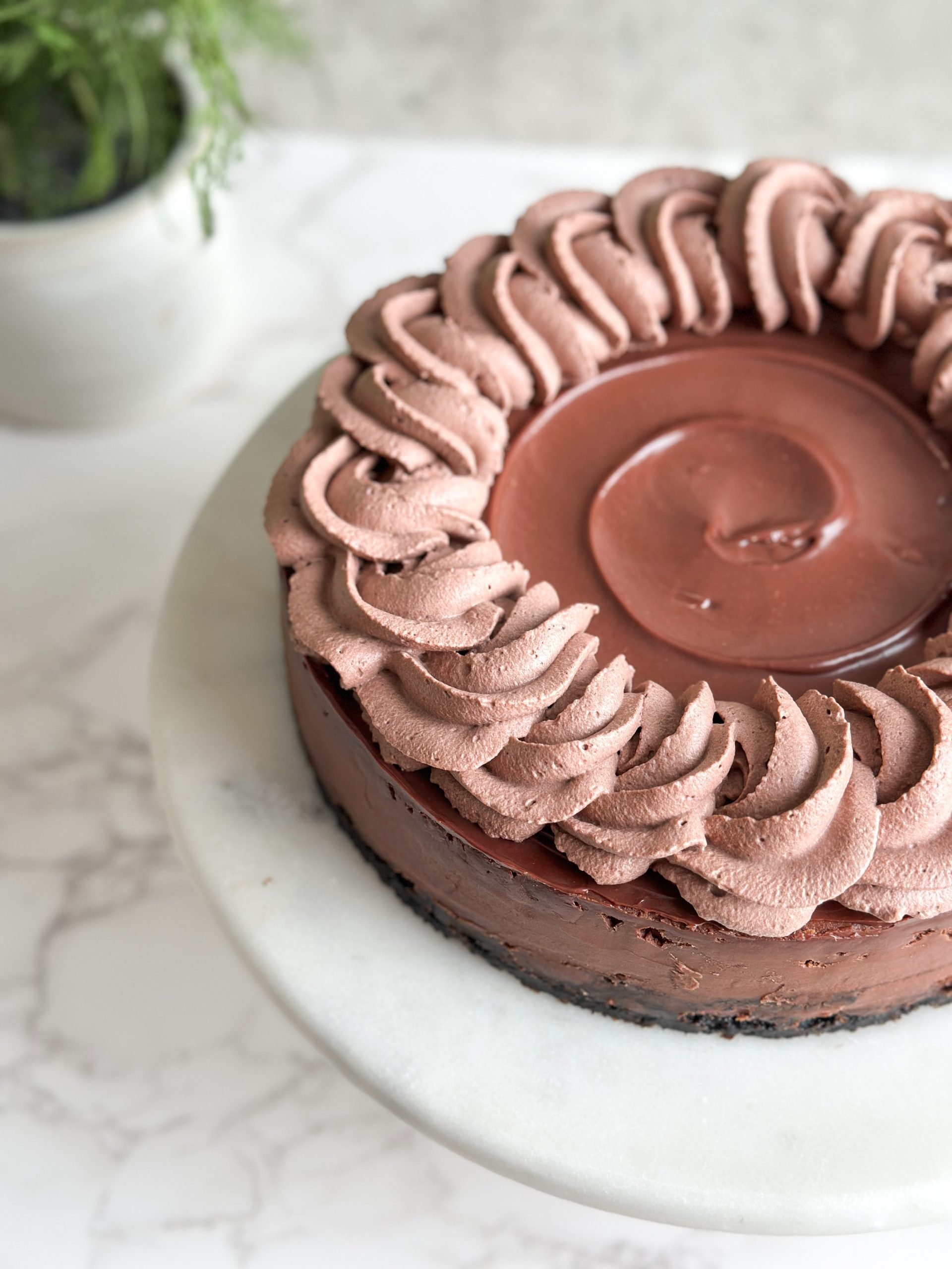 Close up partial image of a chocolate cheesecake on a serving stand with swirled ganache and whipped cream rosettes on it