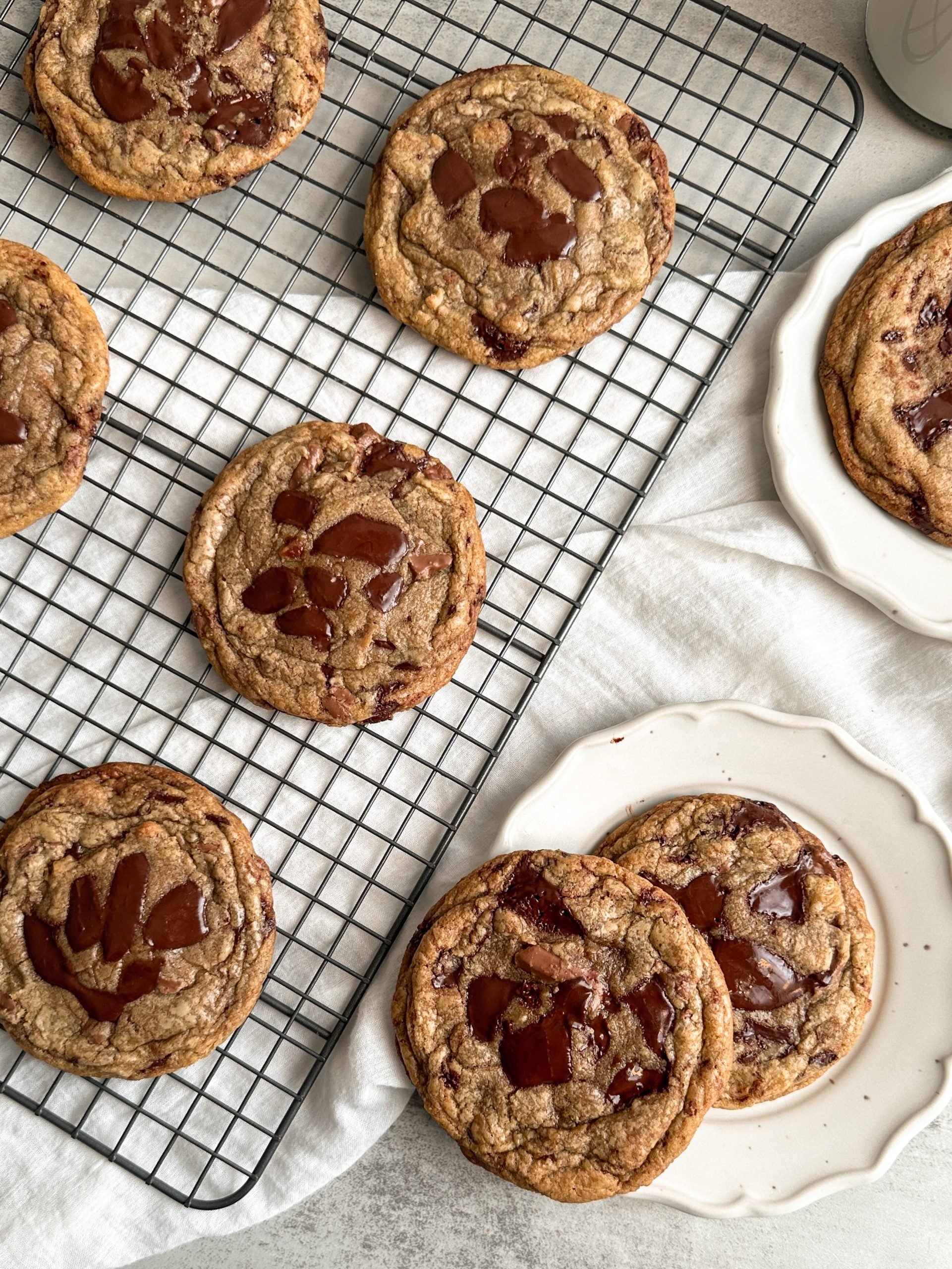 Overhead shot of chocolate chip cookies on a cooling rack, and 2 cookies on a small plate