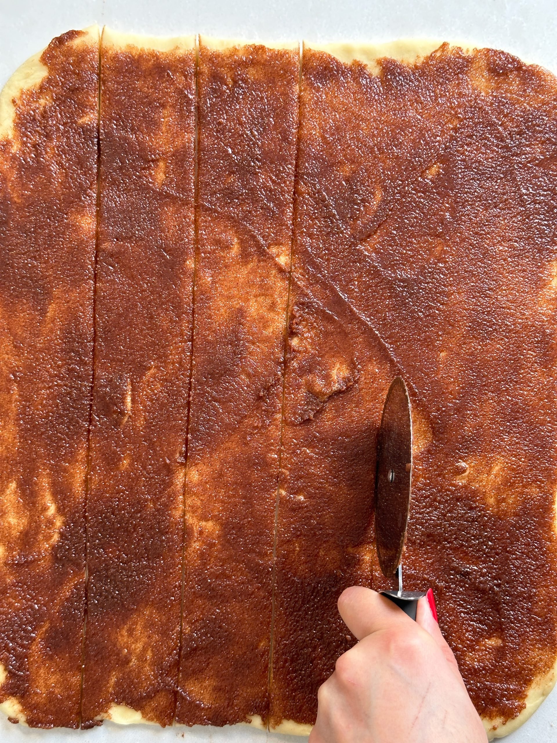 Dough rolled out into a sheet, with cinnamon sugar spread on it. A hand is cutting the dough into strips