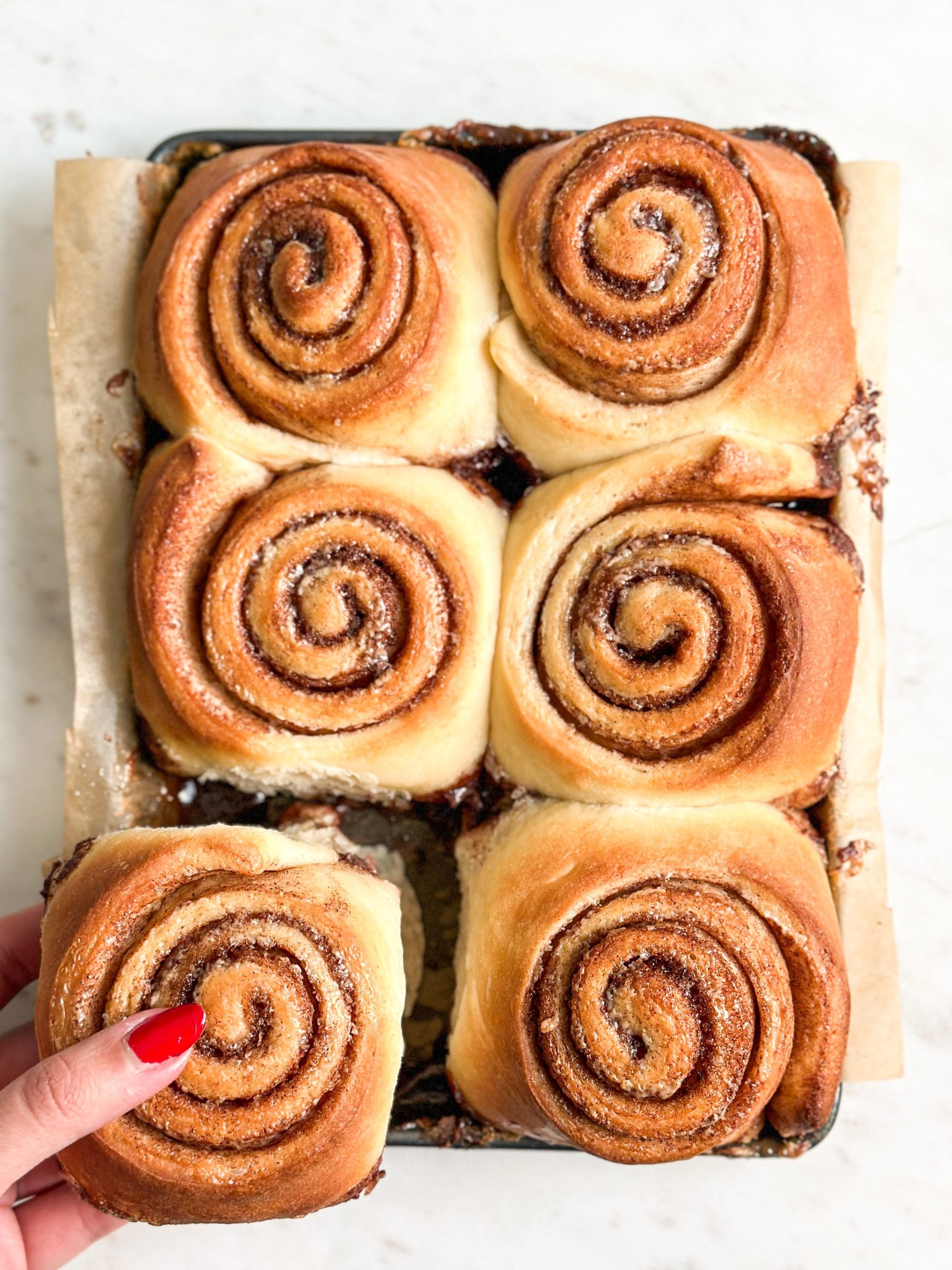 6 cinnamon rolls in a baking tray, with a hand pulling one cinnamon roll apart