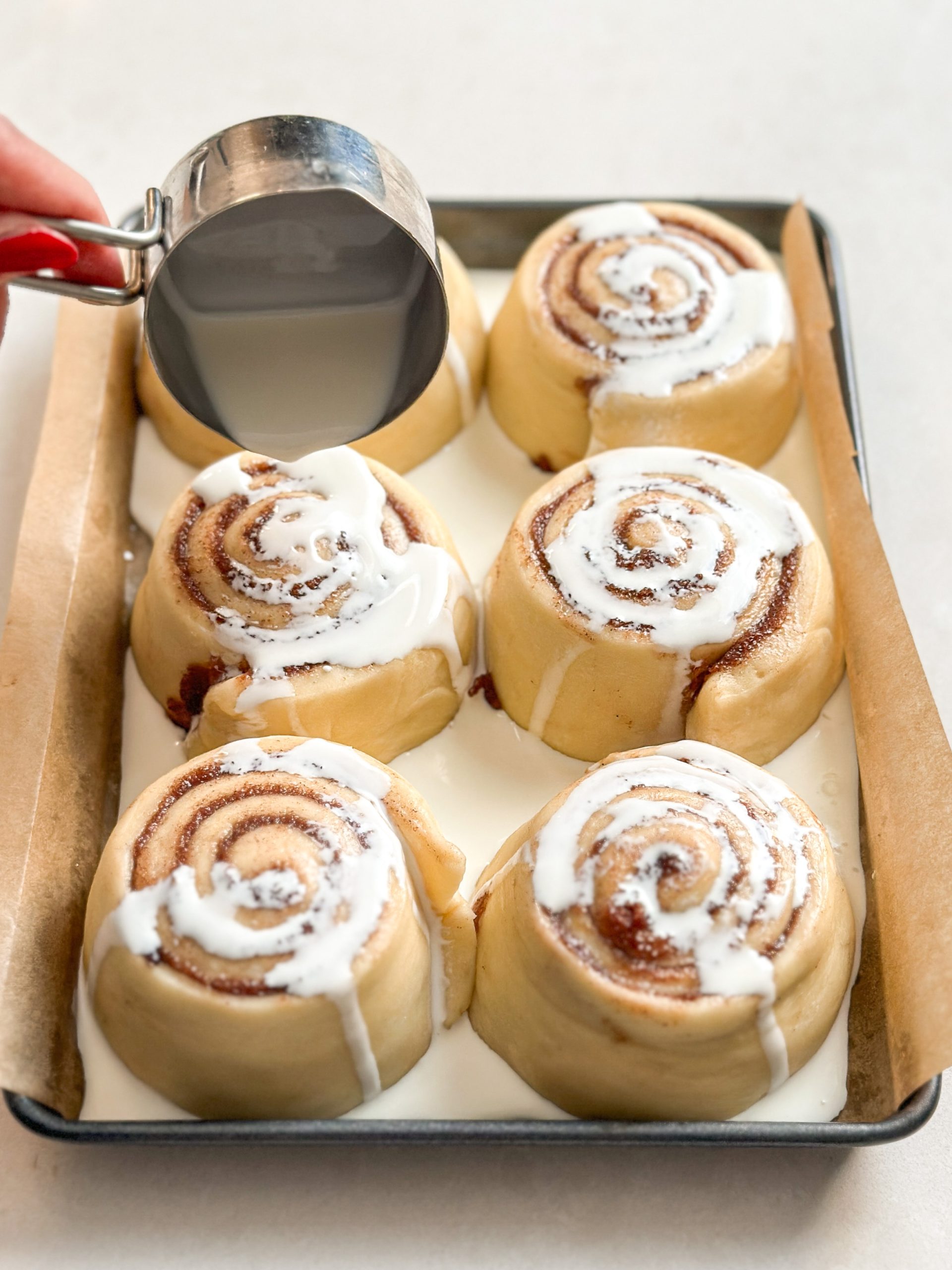 A small batch of 6 uncooked cinnamon rolls, with cream being poured over them