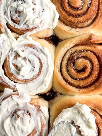 6 cinnamon rolls with cream cheese frosting being spread on them