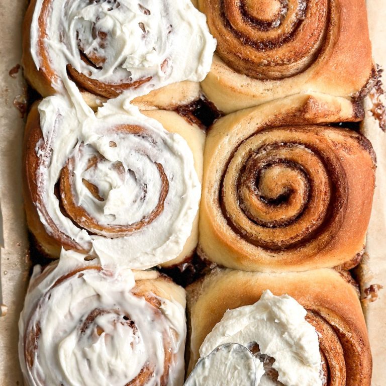 6 cinnamon rolls with cream cheese frosting being spread on them