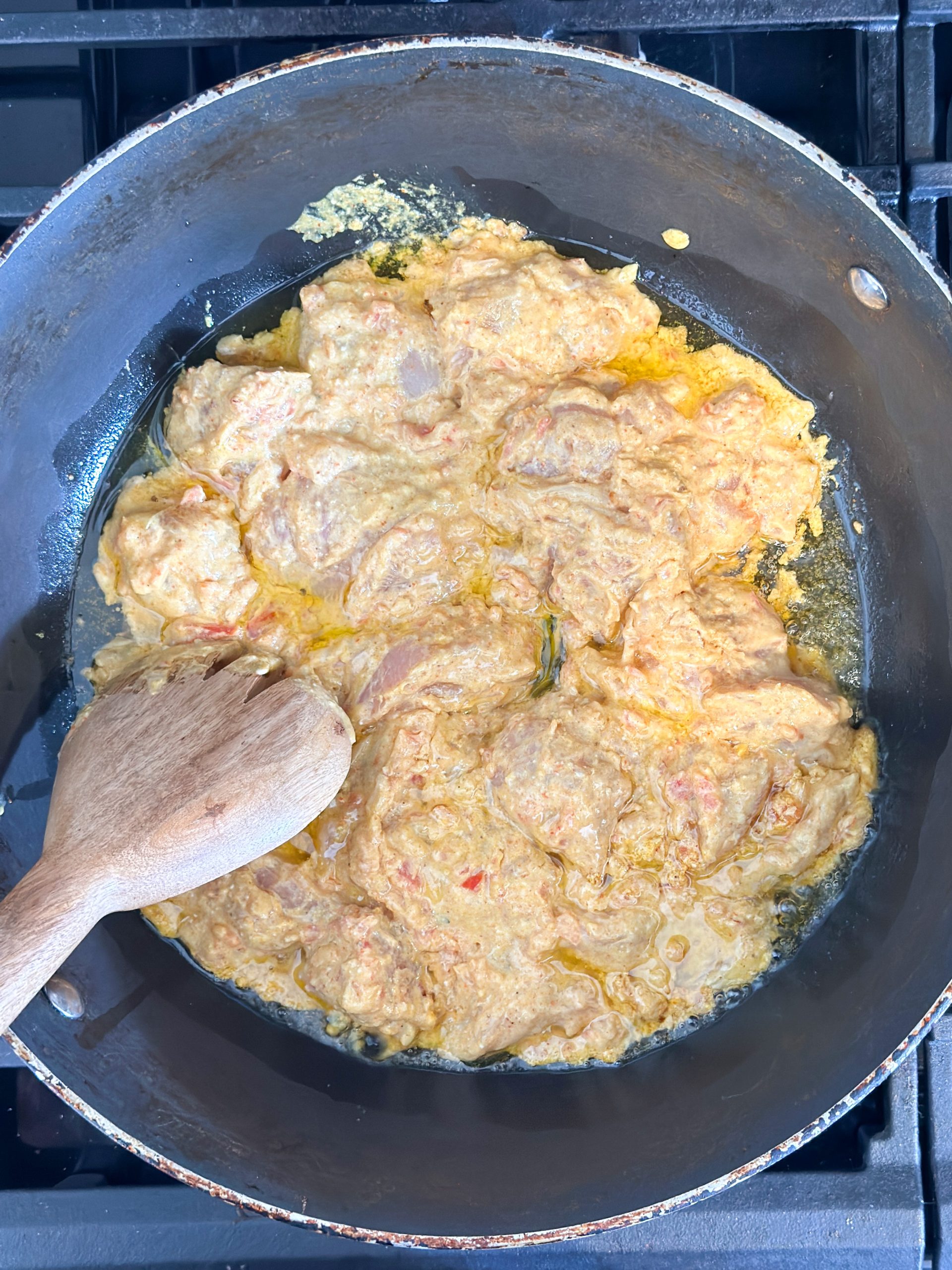 tandoori chicken being cooked in a wok with a wooden spoon mixing it