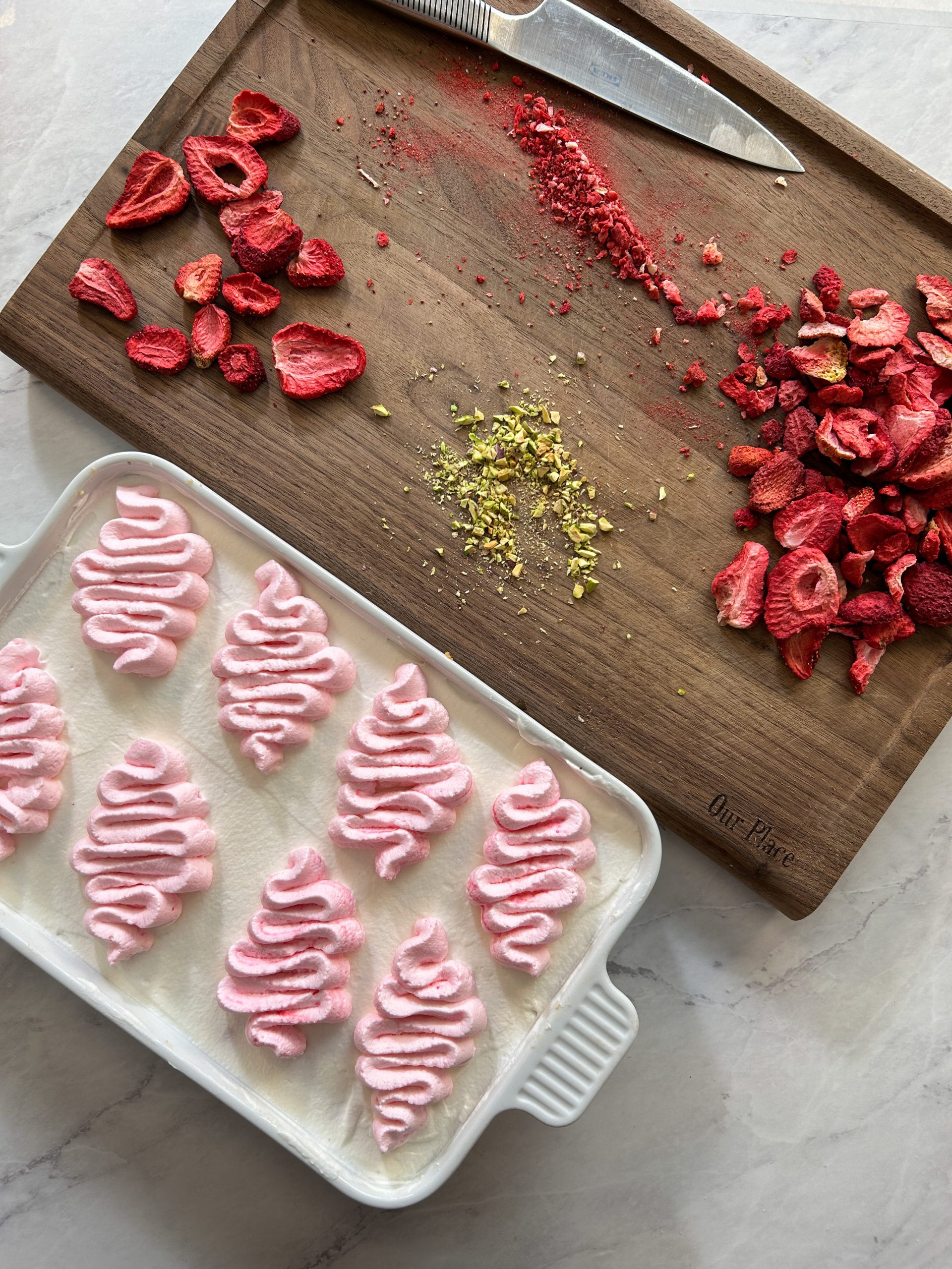 overhead picture showing a dish with tres leches cake next to a cutting board with chopped freeze dried strawberries and pistachios