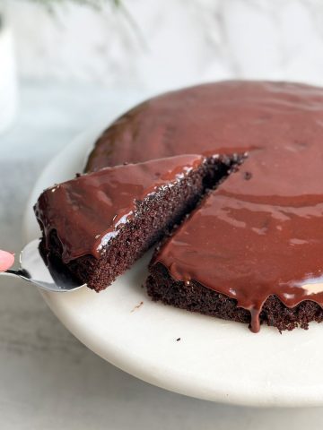Moist chocolate cake with a shiny chocolate ganache, spatula taking out one slice from the cake