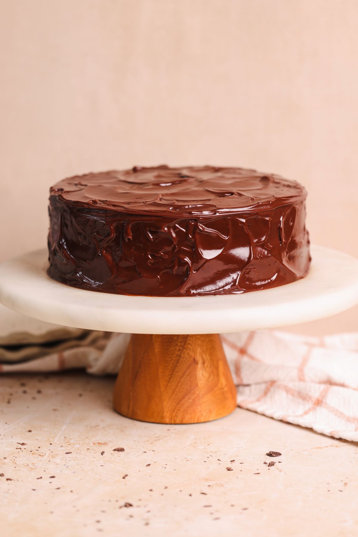 a chocolate cake on a marble cake stand covered in a shiny ganache frosting