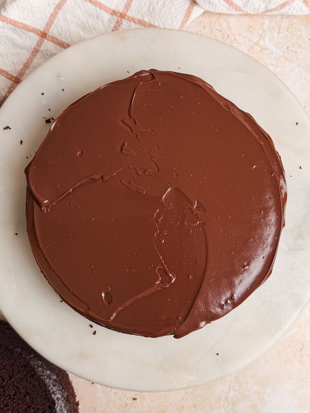 ganache spread on top of layer of chocolate cake on a marble cake stand