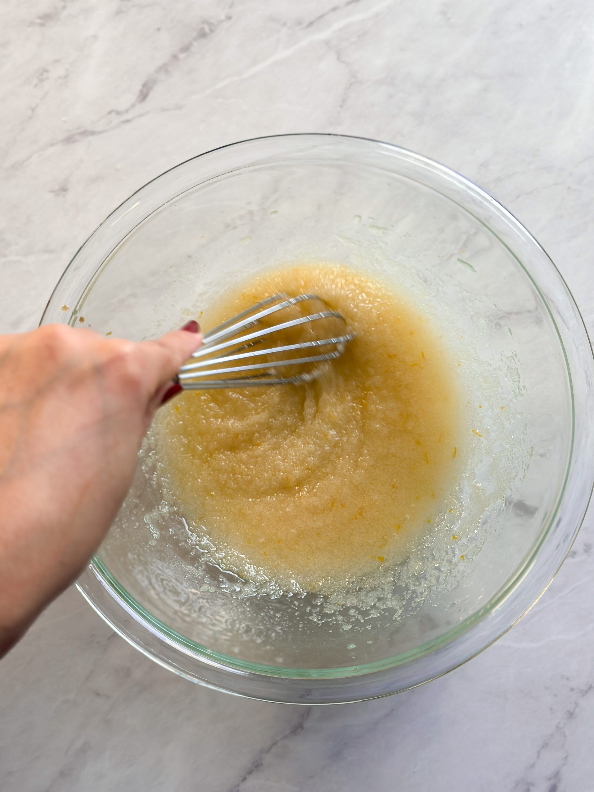 Hand is whisking butter, oil and sugar in a glass bowl