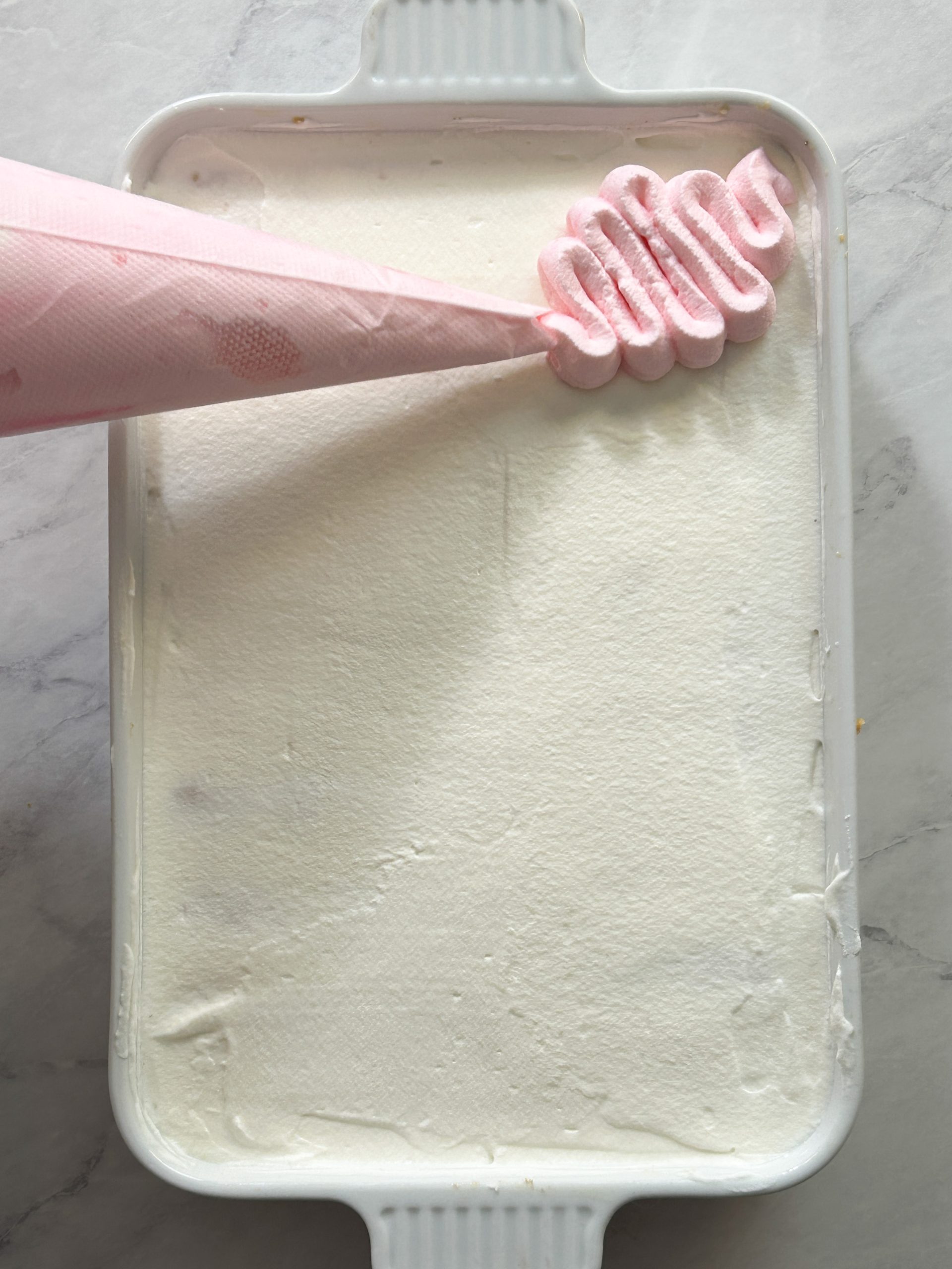 piping bag with pink whipped cream is piping a swirl onto tres leches cake
