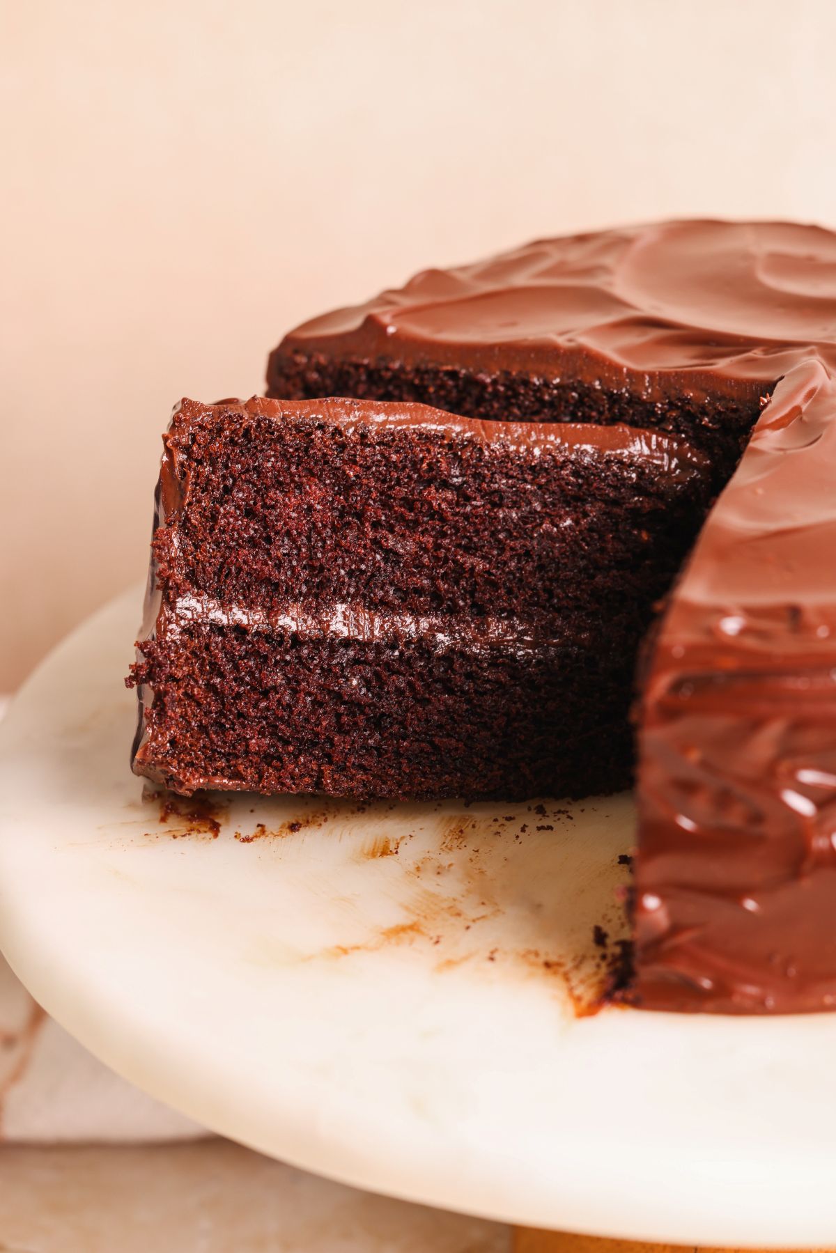 close up of a slice of chocolate cake resting against the cake, with 2 layers and ganache