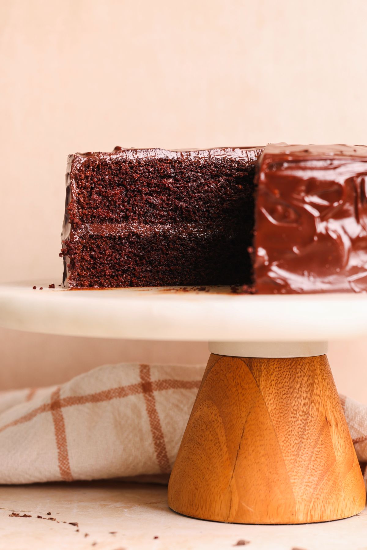 a chocolate cake on a marble cake stand with some slices removed to show the cross section. cake has 2 layers and shiny chocolate ganache frosting
