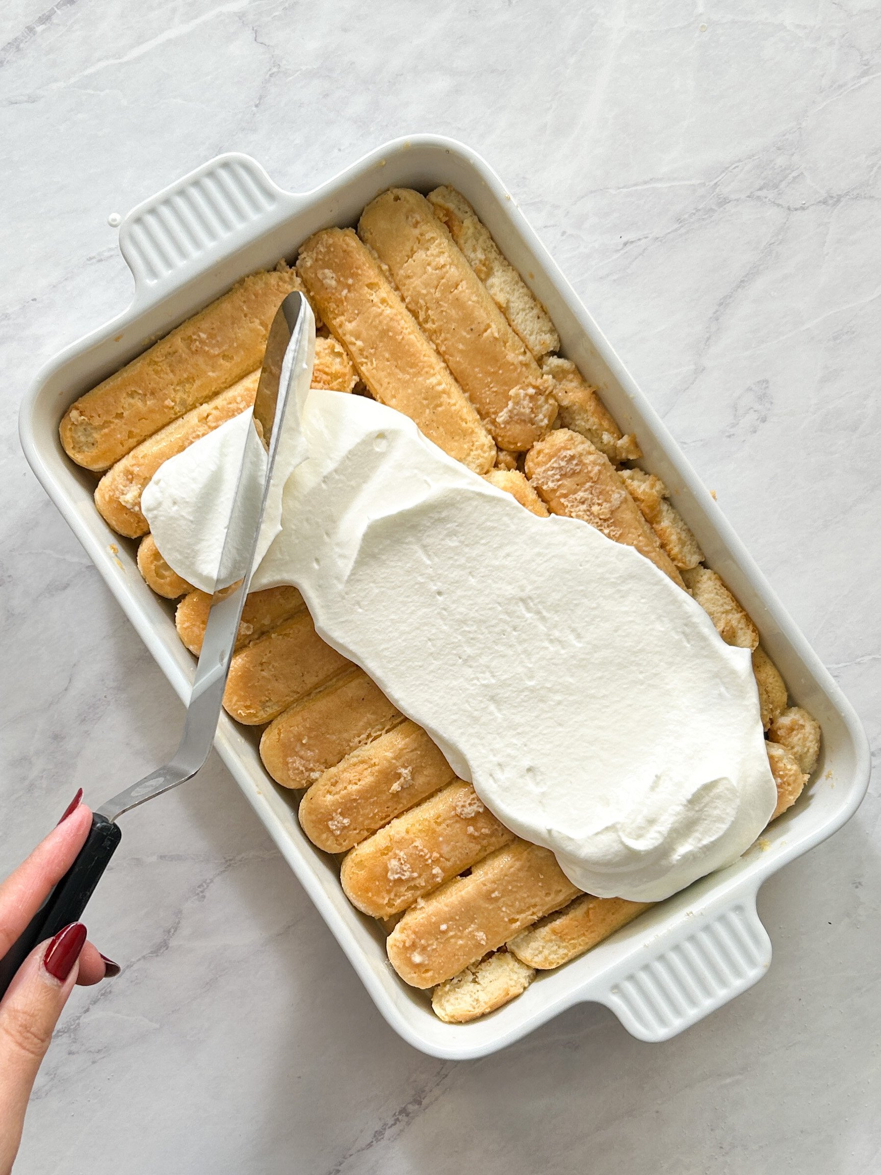 offset spatula being used to spread whipped cream onto tres leches cake