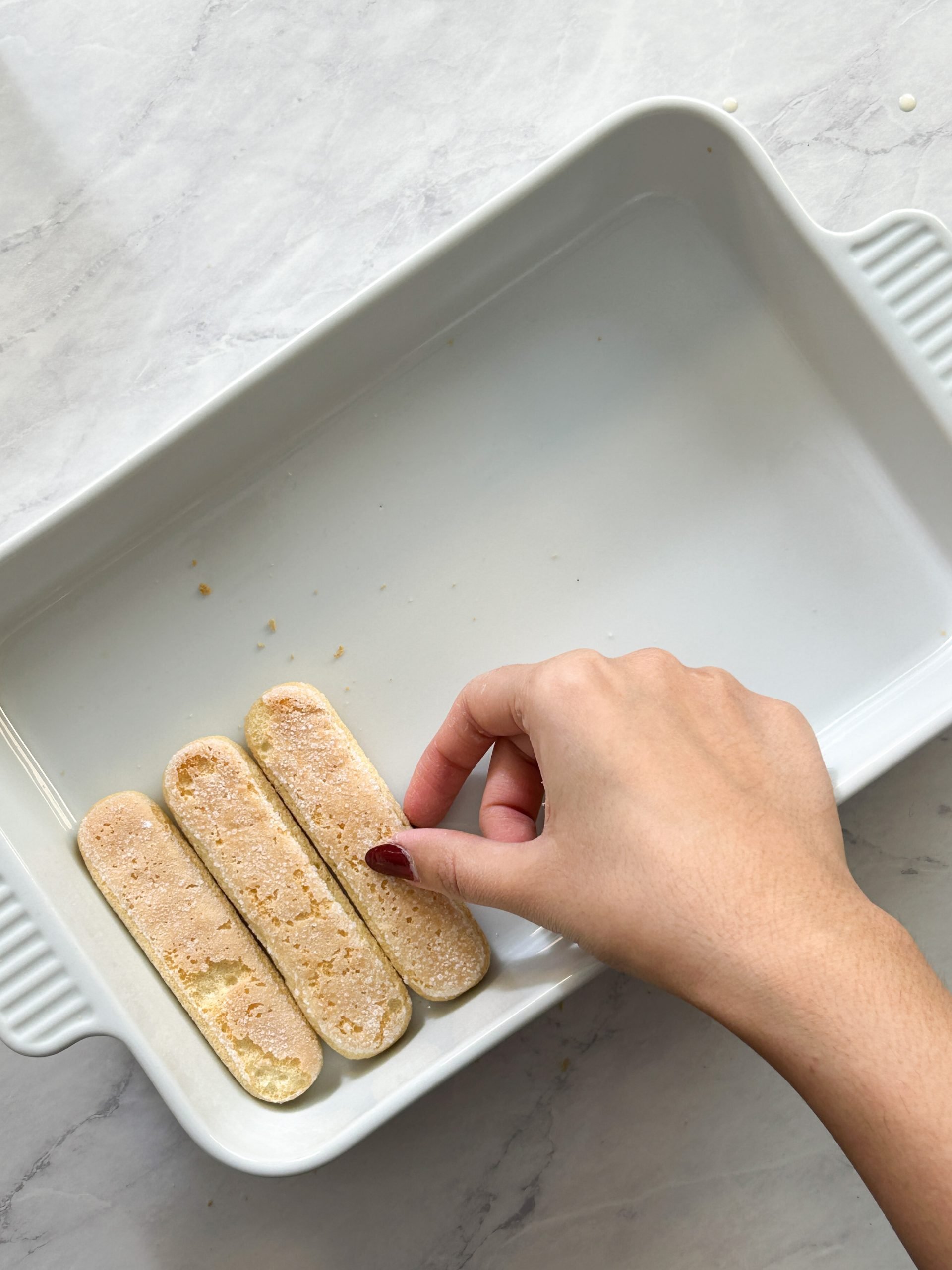 hand is stacking ladyfingers in a rectangle ceramic dish side by side