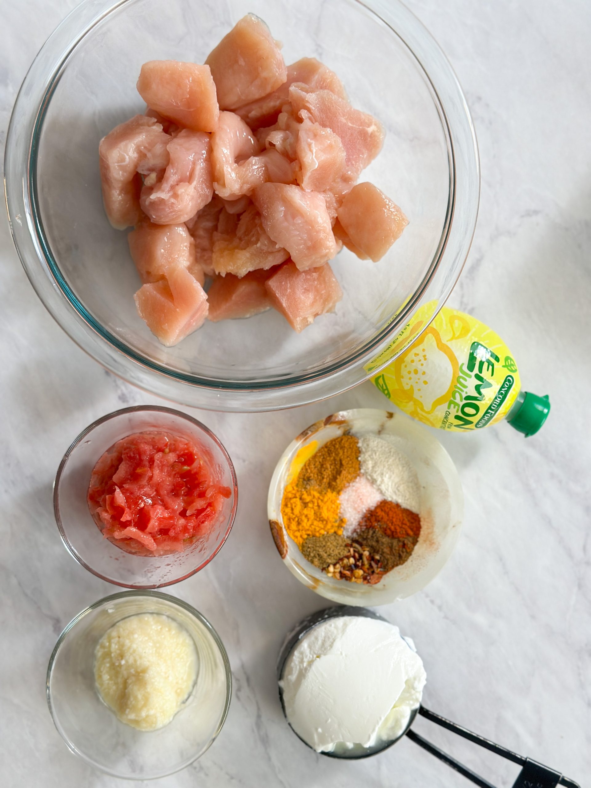 an overhead image of different ingredients: boneless cubed chicken, spices, yogurt, tomato, garlic ginger and lemon juice