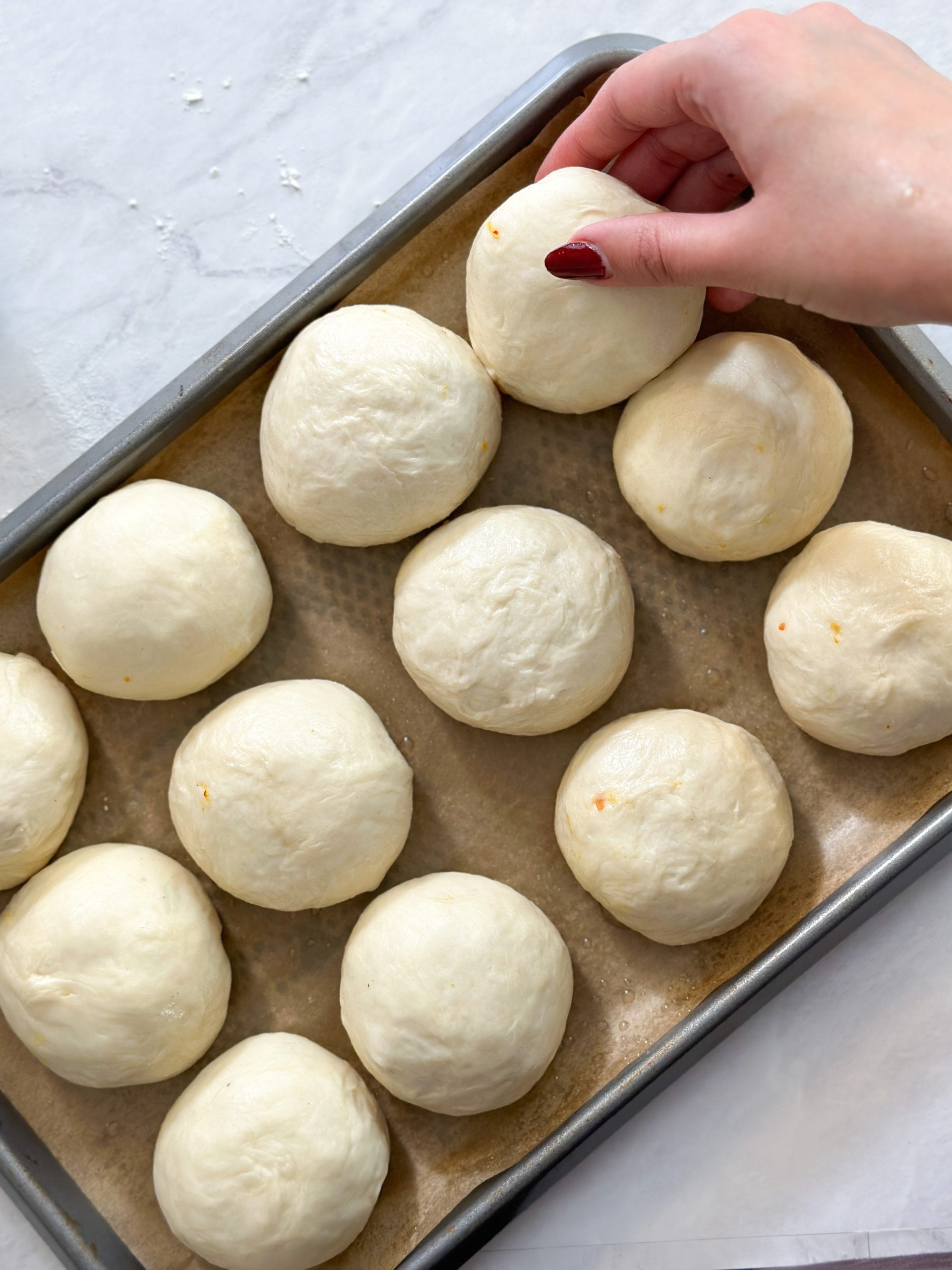 hand is placing a naan bun in a tray with 11 other naan buns, to have 12 overall