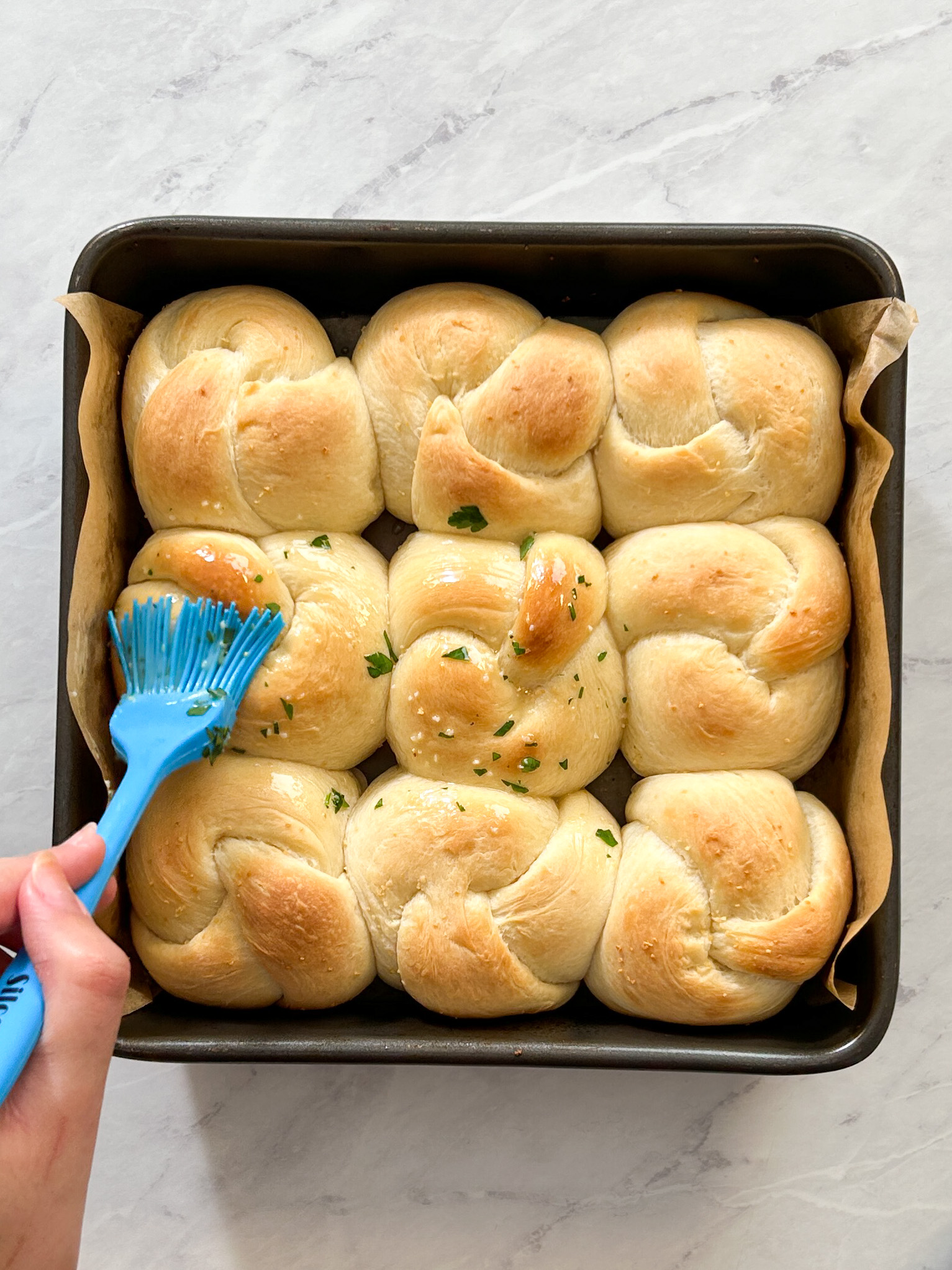 a pastry brush is brushing garlic butter onto baked garlic knots