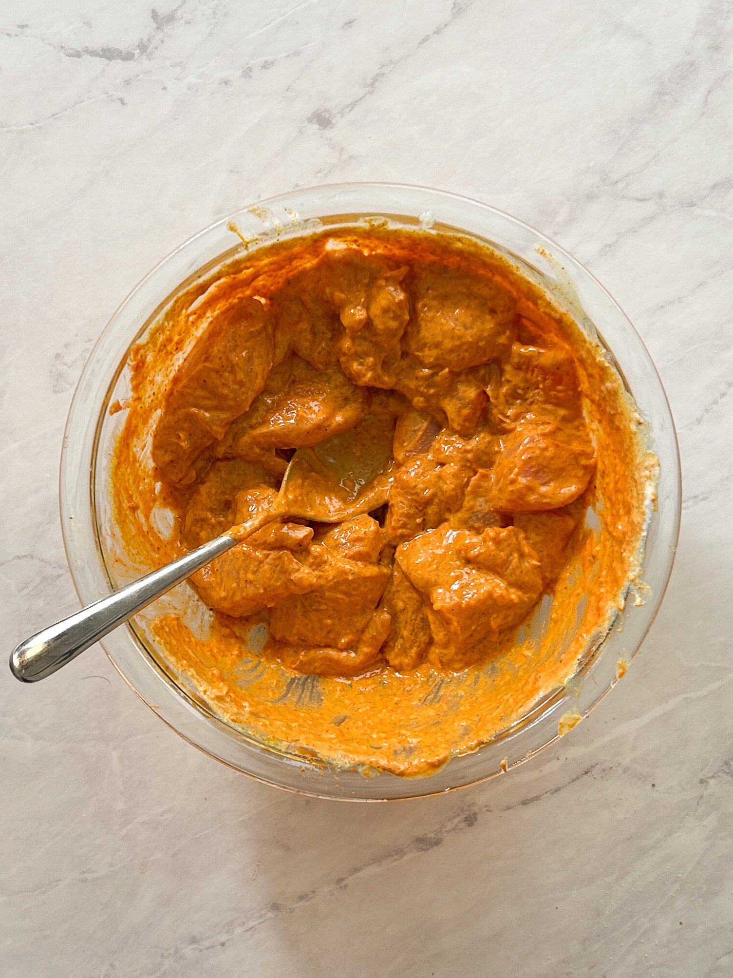 chicken tikka being marinated in a glass bowl