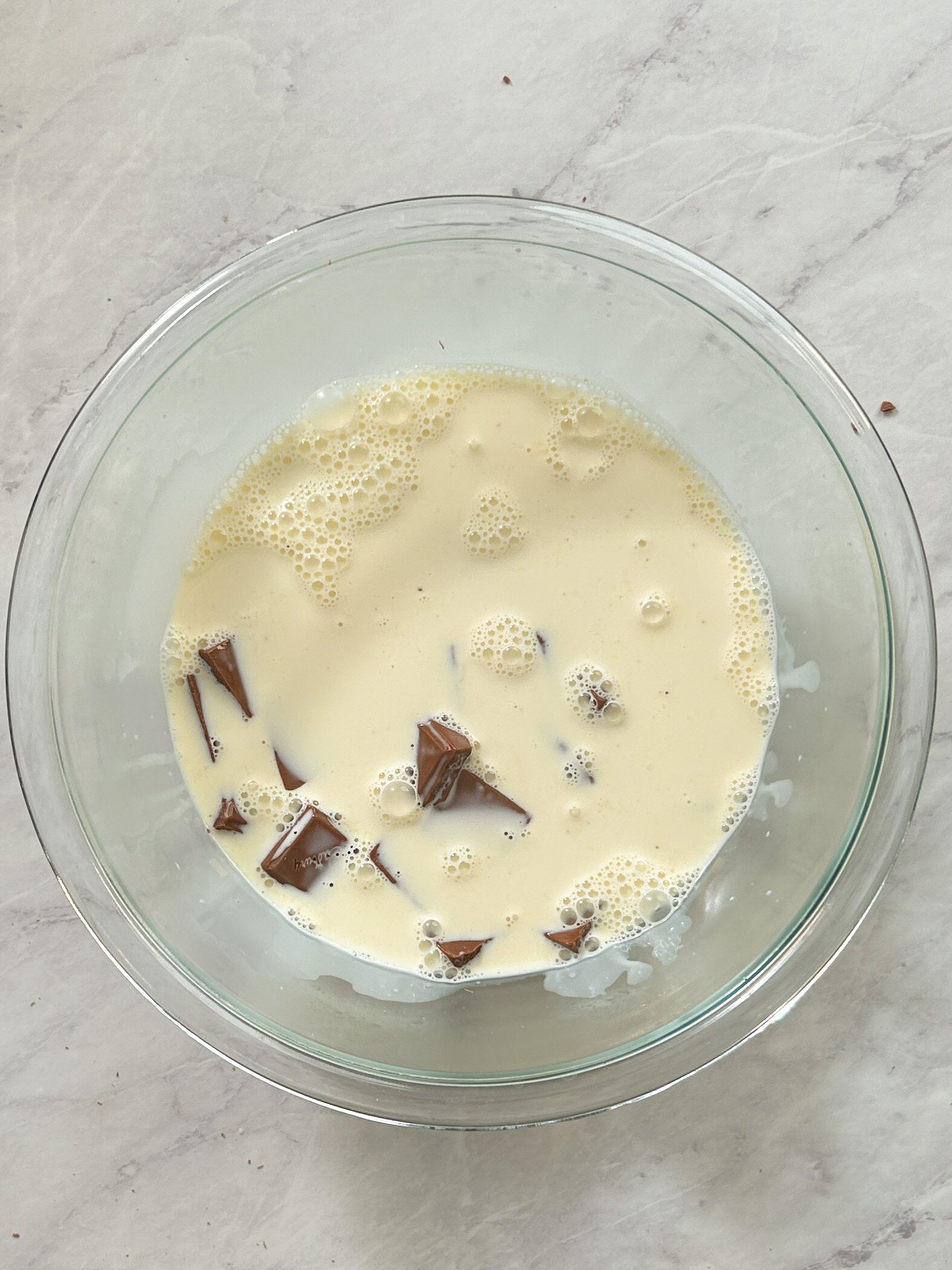 hot cream poured over chocolate chunks in a glass bowl