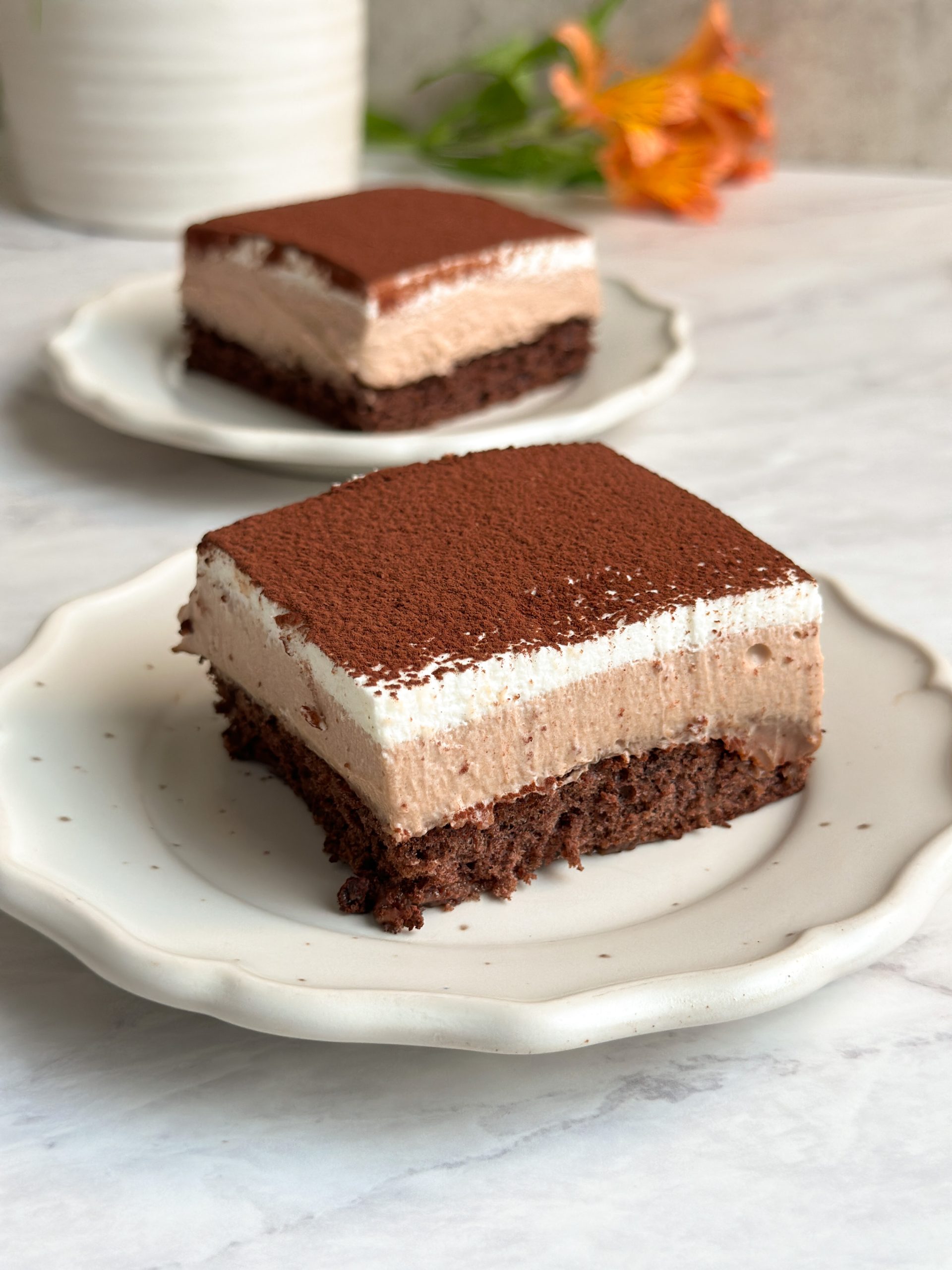 square slice of chocolate mousse cake on a small plate with layers of cake, mousse and whipped cream