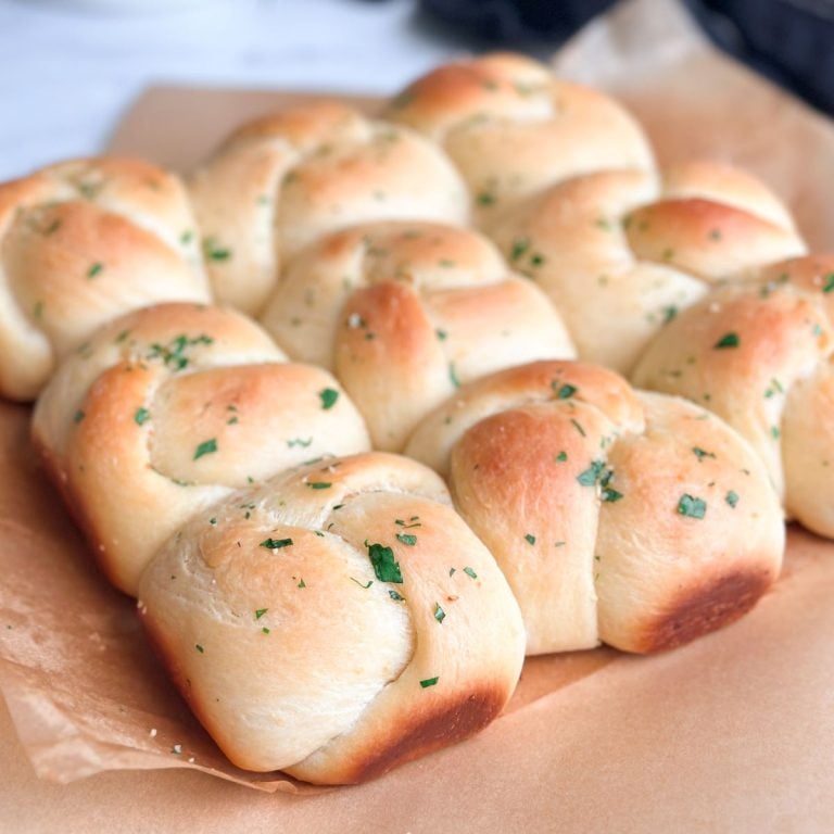 9 garlic knots in a batch touching each other. They are golden in color and brushed with garlic butter and parsley