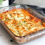 chicken alfredo lasagna in a dish. lasagna has a beautiful golden cheesy crust and is garnished with chopped parsley