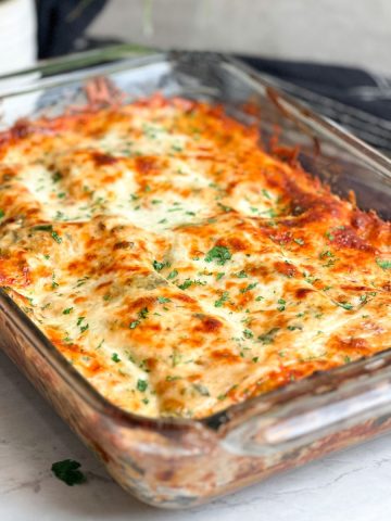 chicken alfredo lasagna in a dish. lasagna has a beautiful golden cheesy crust and is garnished with chopped parsley
