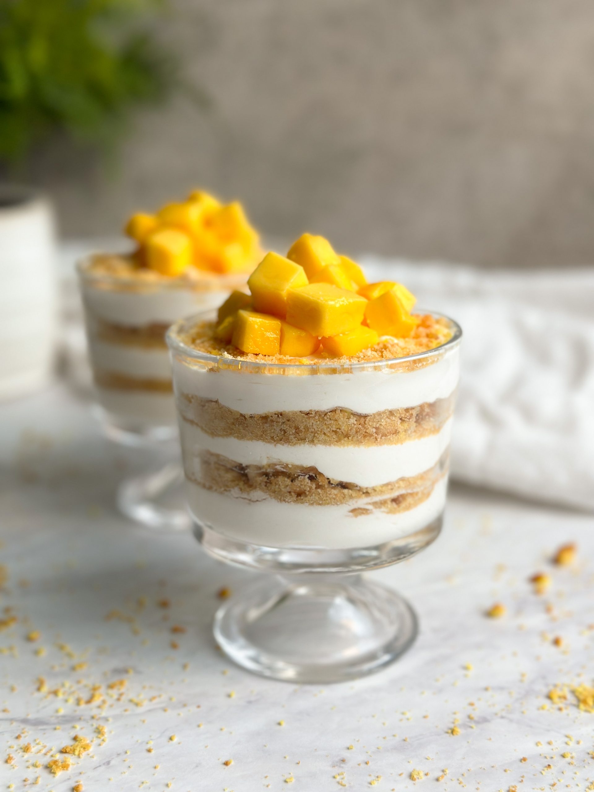 2 cups of yogurt parfait dessert with layers of yogurt and biscuits, topped with chopped mango