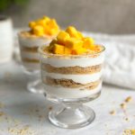 2 cups of yogurt parfait dessert with layers of yogurt and biscuits, topped with chopped mango