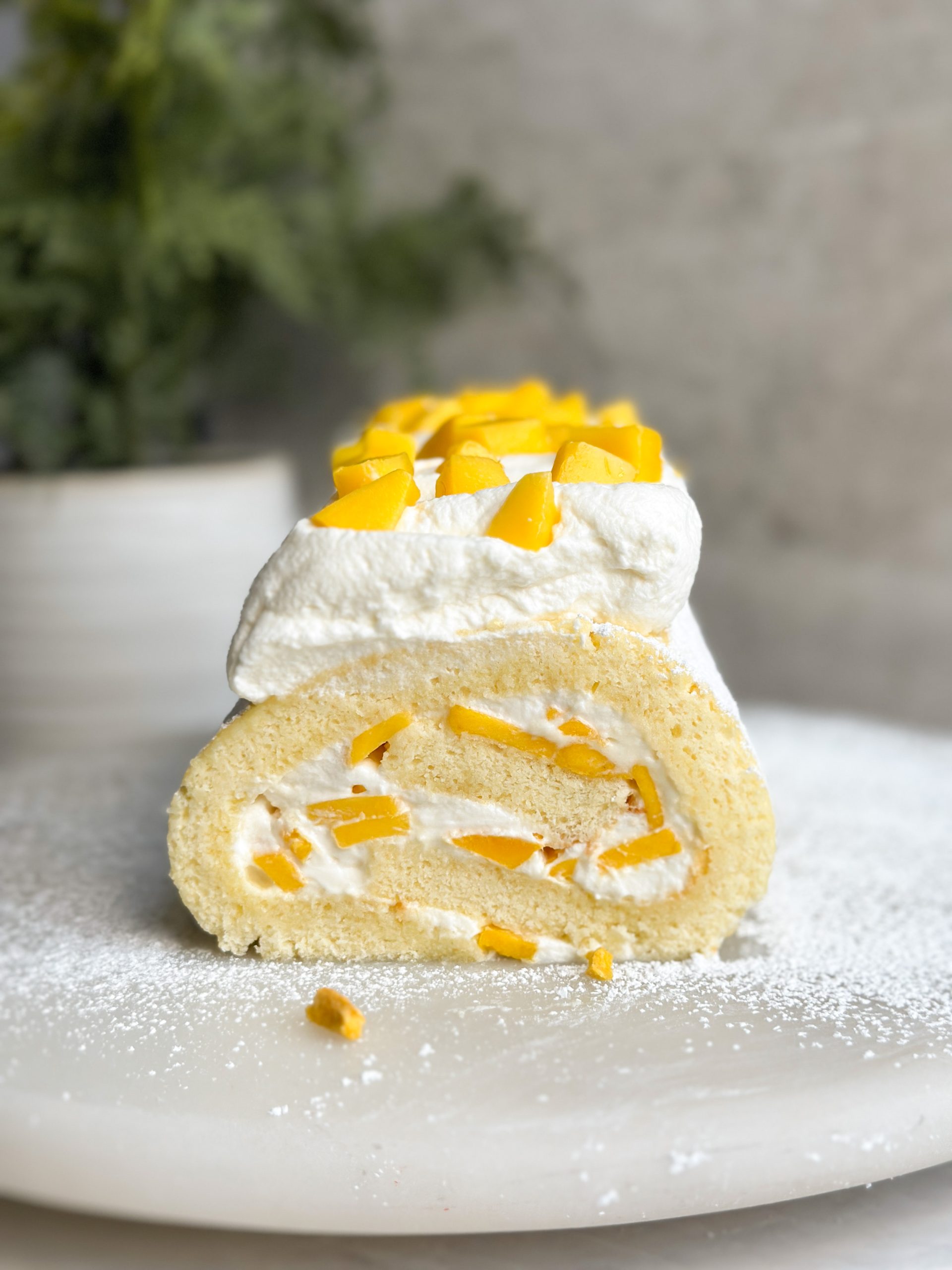 mango chantilly swiss roll on a serving stand with a clear swirl of cake, cream and mango visible