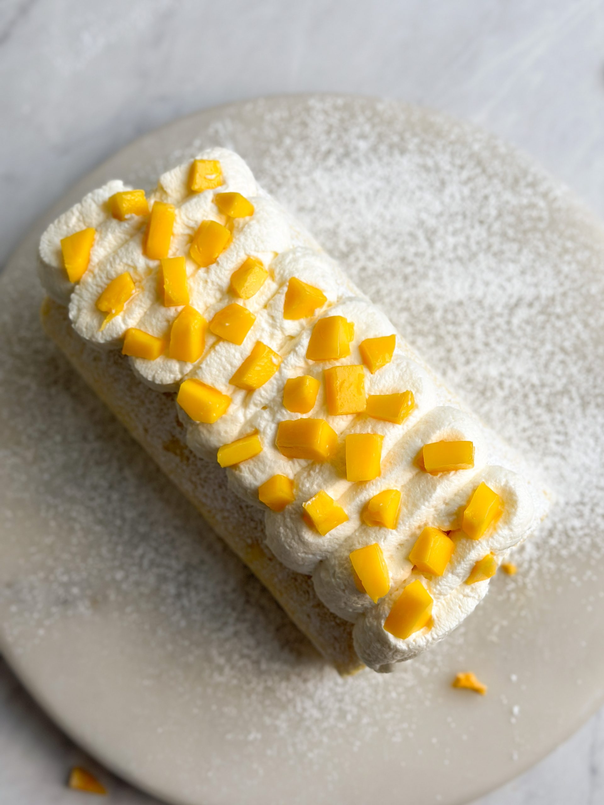 overhead picture of mango swiss roll cake with swirls of chantilly cream and cubed mango