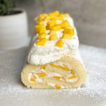 mango and cream swiss roll decorated with whipped cream and chopped mangoes. picture from the front SHOWING THE CROSS SECTION WITH A SWIRL OF CAKE AND CREAM